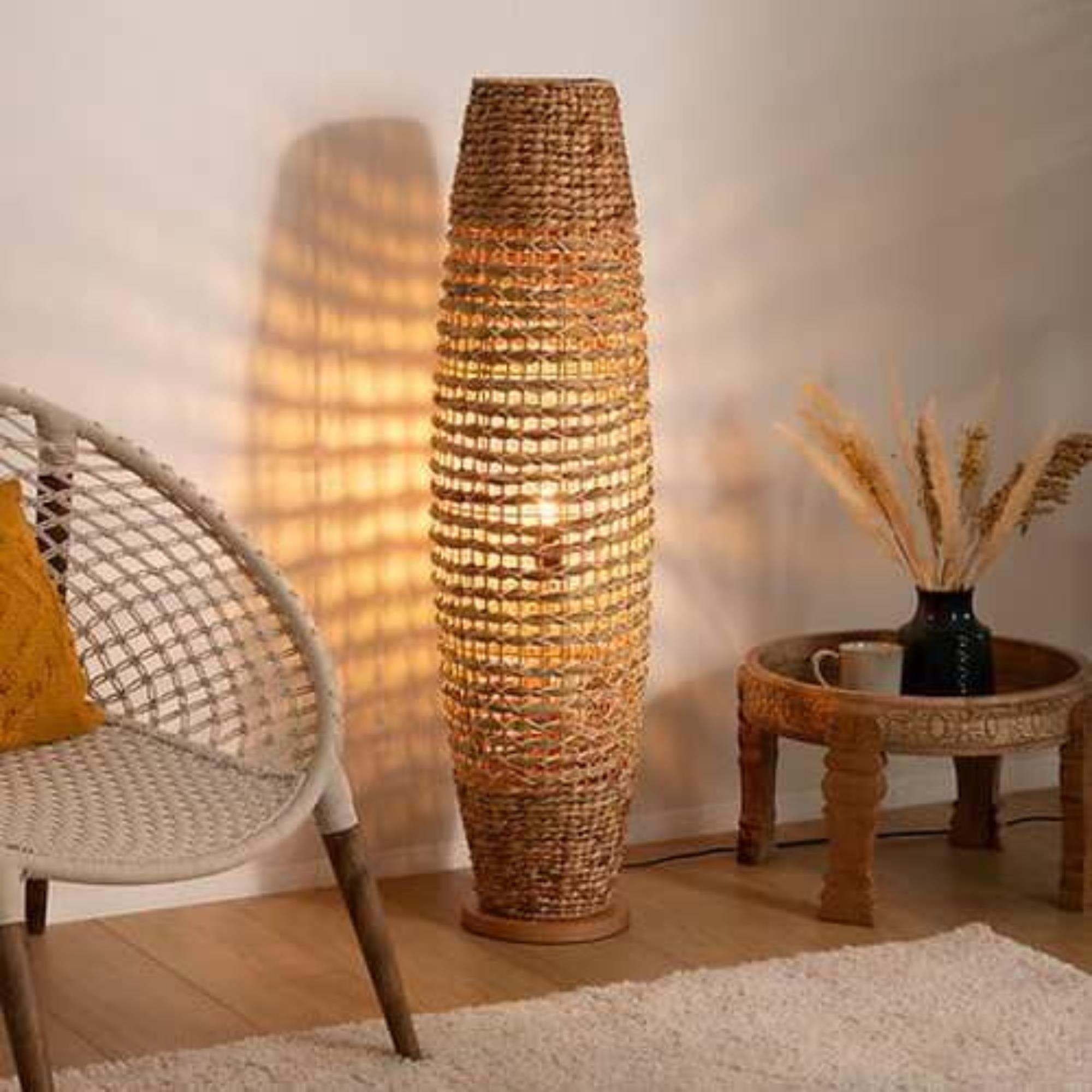 Una lámpara de pie tejida se alza junto a una silla blanca y una mesa de madera.