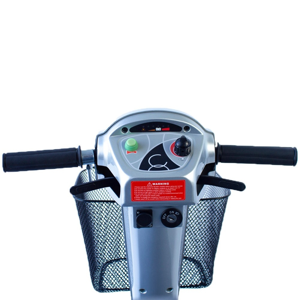 Vista frontal de la consola de un scooter plateado con manillar, cesta, etiqueta de advertencia y controles.