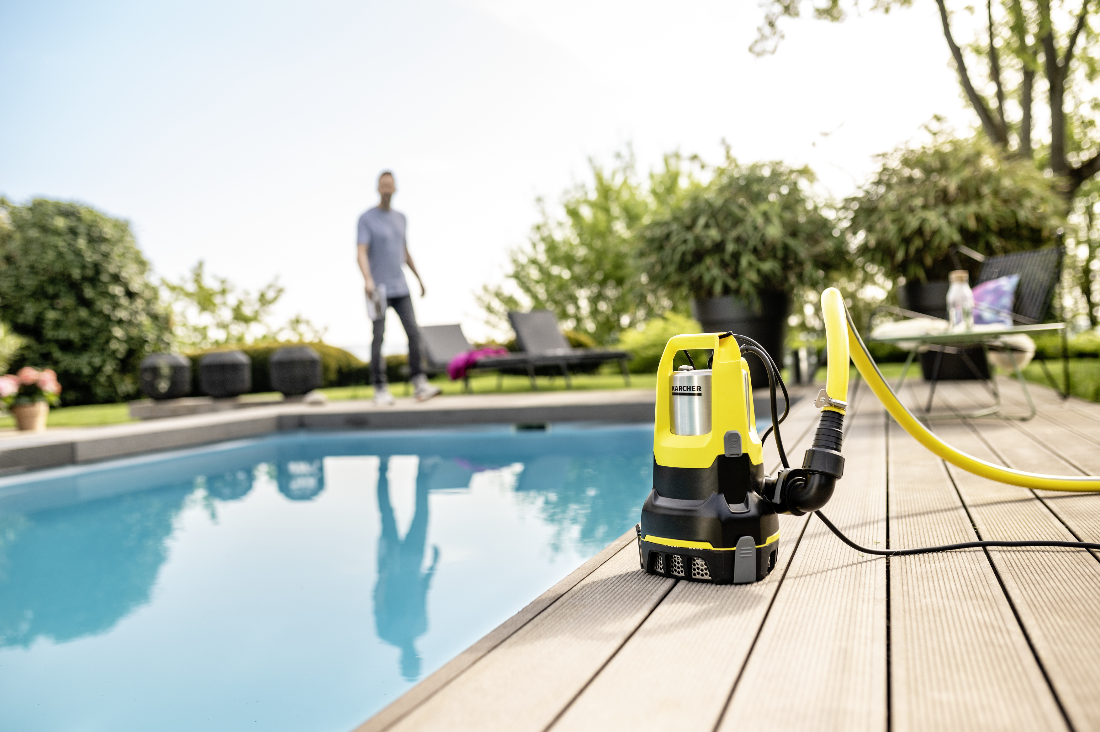 Żółta pompa zanurzeniowa z wężem na drewnianym tarasie przy basenie.