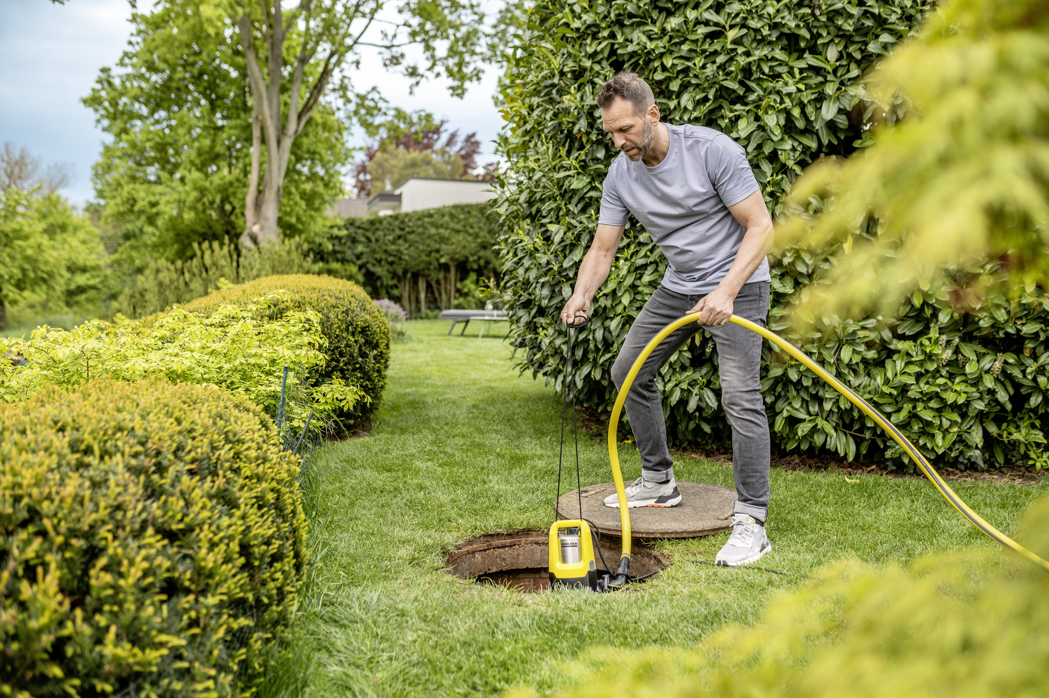 Mężczyzna z żółtym wężem pompującym wodę z ogrodu.