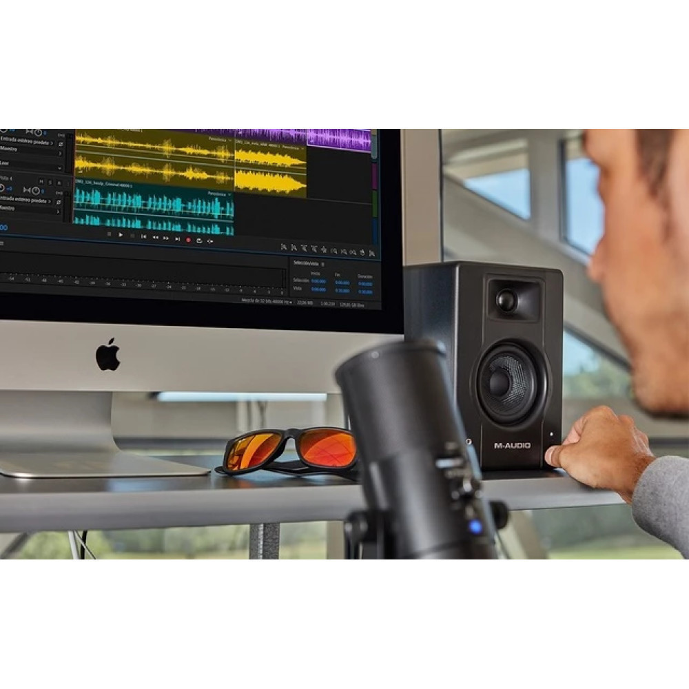 Mężczyzna dotyka głośnika obok ekranu Mac z oprogramowaniem audio.