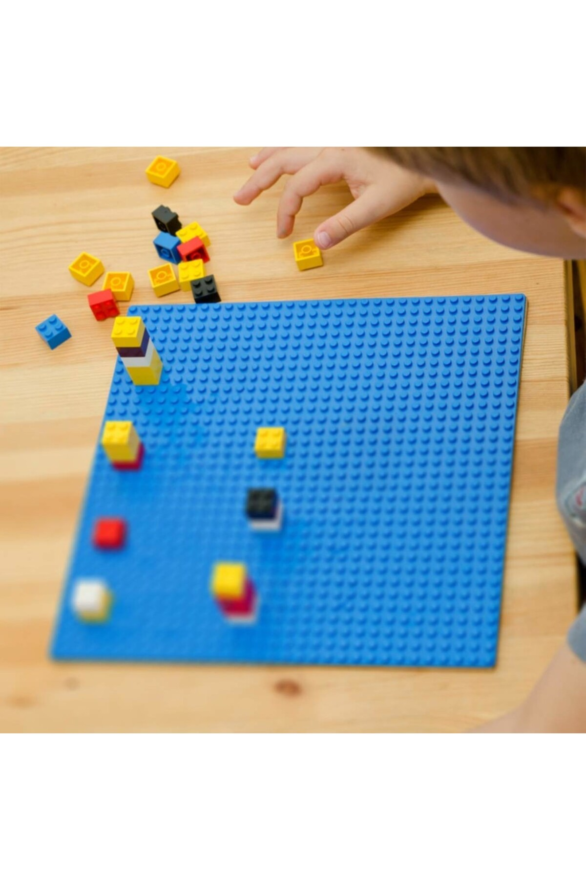Bir çocuk mavi Lego zemininde renkli Lego tuğlalarıyla oynuyor.
