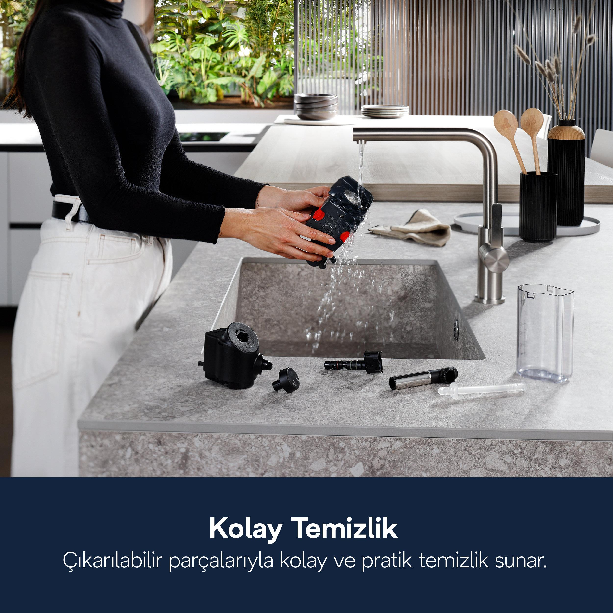 Bir kişi modern bir mutfakta akan su altında cihaz parçalarını temizliyor.