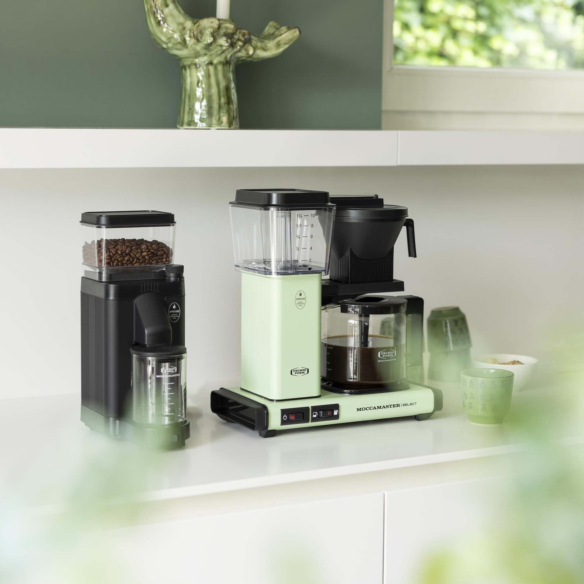 Młynek do kawy i ekspres do kawy. Jasnozielona maszyna z szklanym dzbankiem, białe tło.