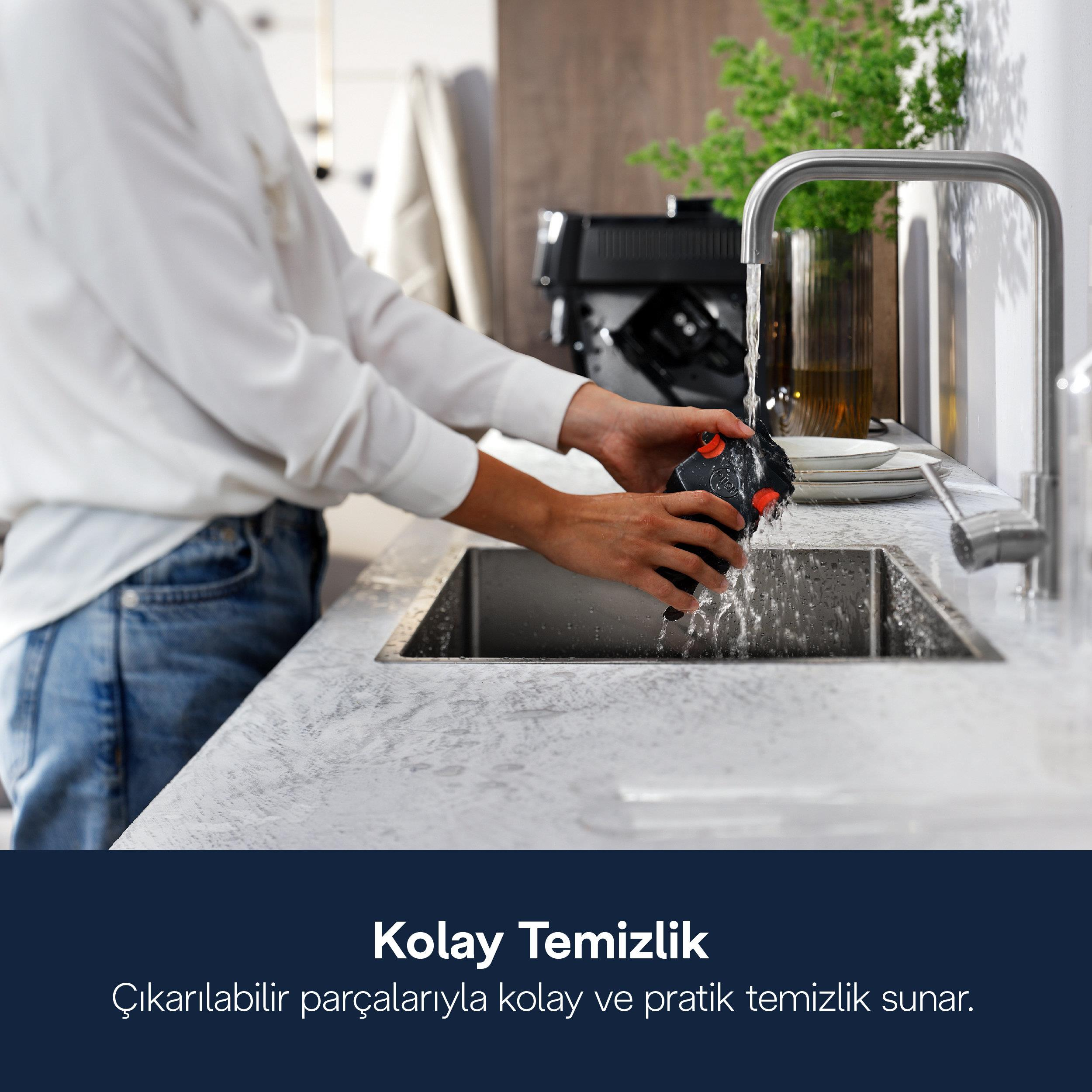 Bir kişi, lavaboda akan su altında kırmızı detaylı siyah bir cihaz yıkıyor.