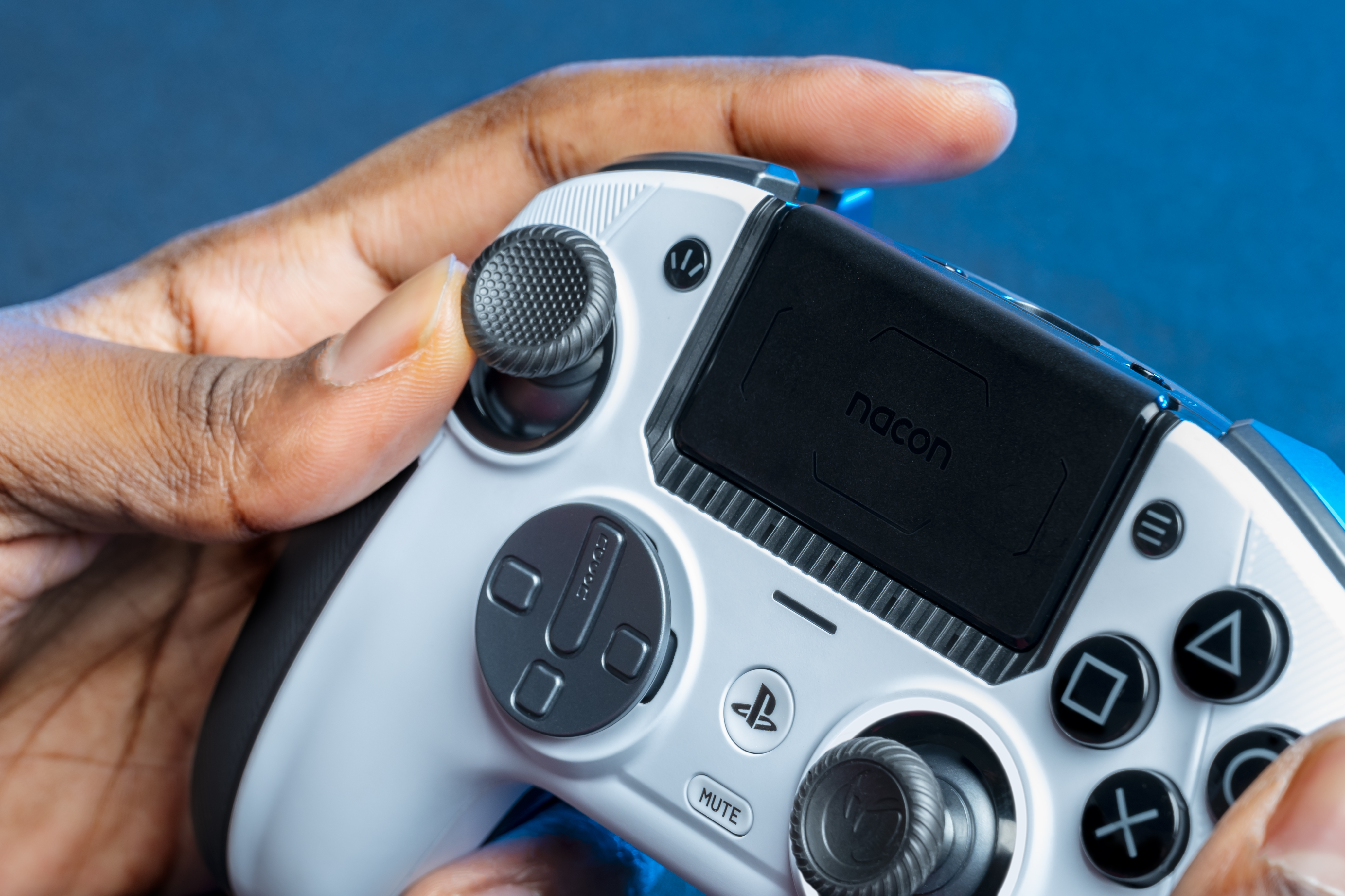 Dłoń trzyma biało-czarny kontroler do gier z niebieskimi akcentami.