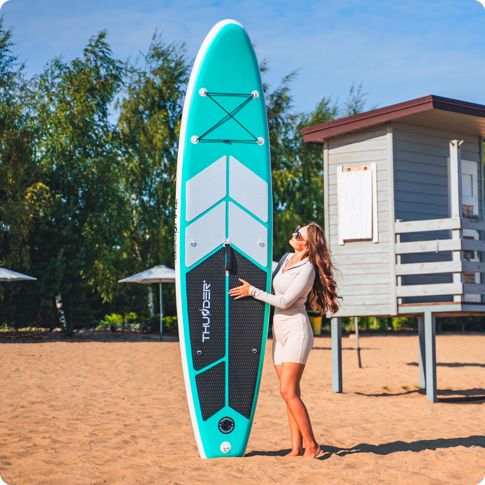 Kobieta z deską SUP na plaży obok wieży ratownika.