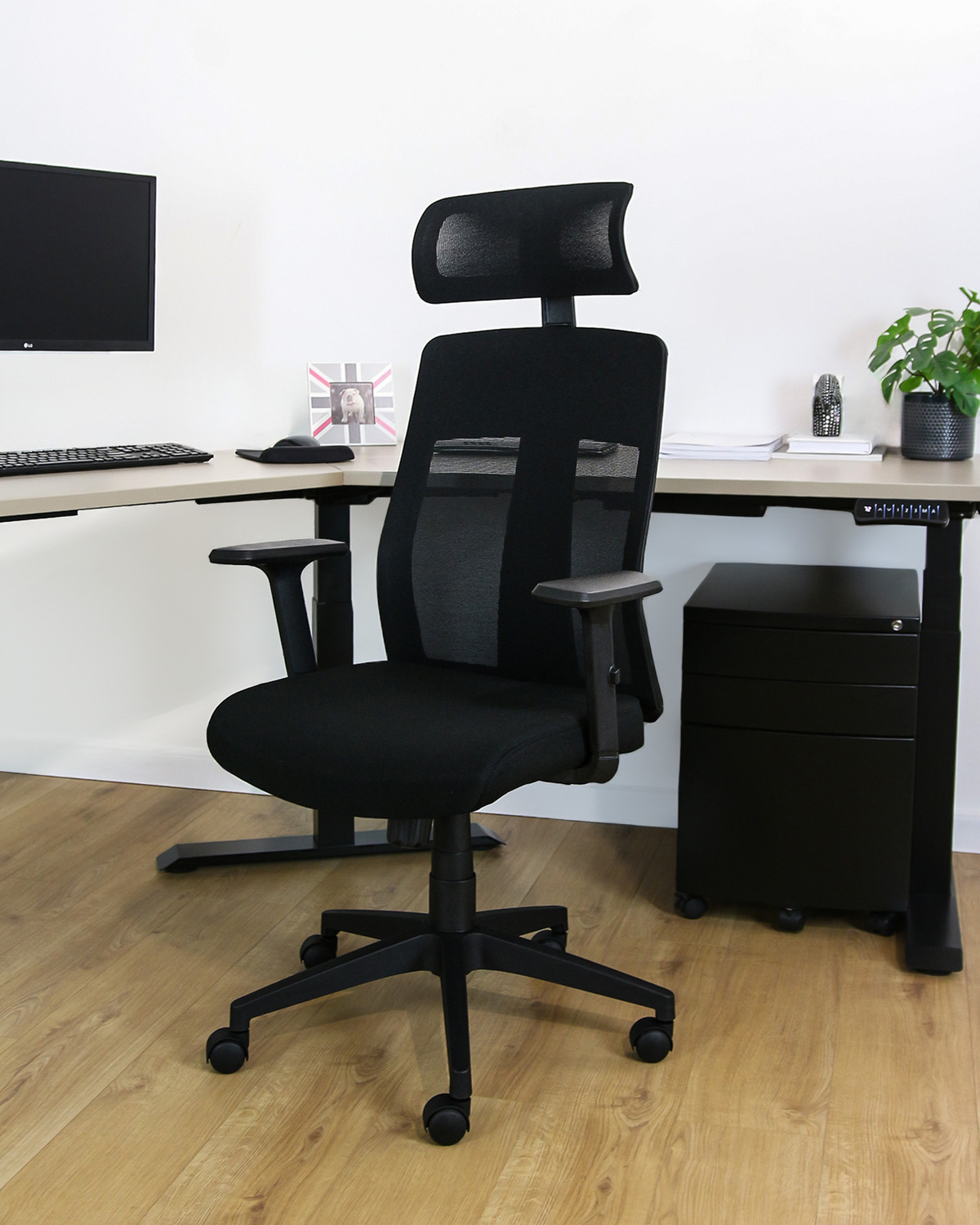 Czarny fotel biurowy z siatkowym oparciem i regulowanymi podłokietnikami na drewnianej podłodze.