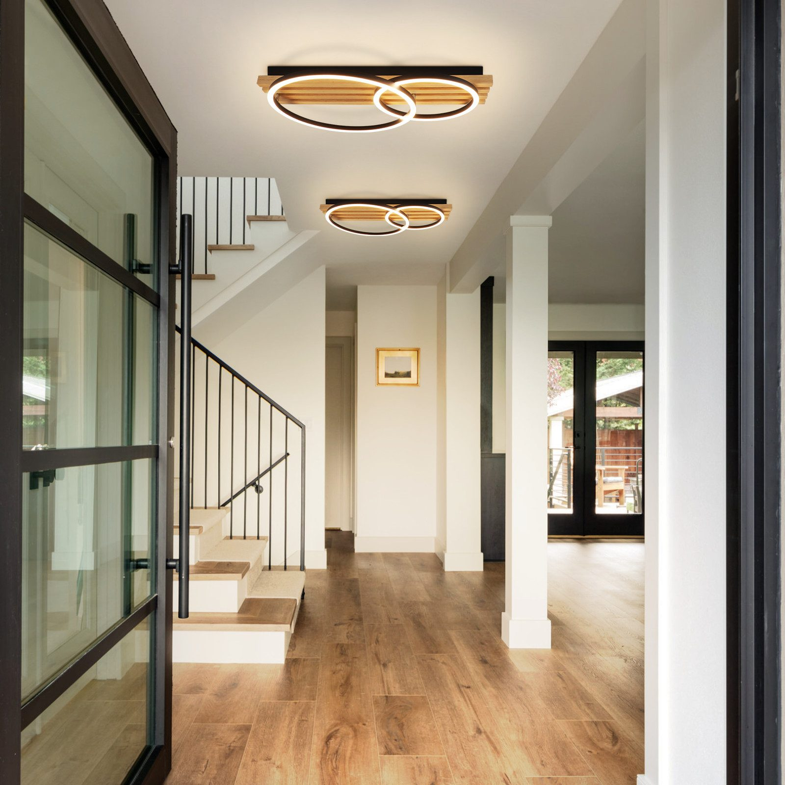 Moderner Flur mit Holzfußboden, Treppe, zwei Ringlampen und Glastür.