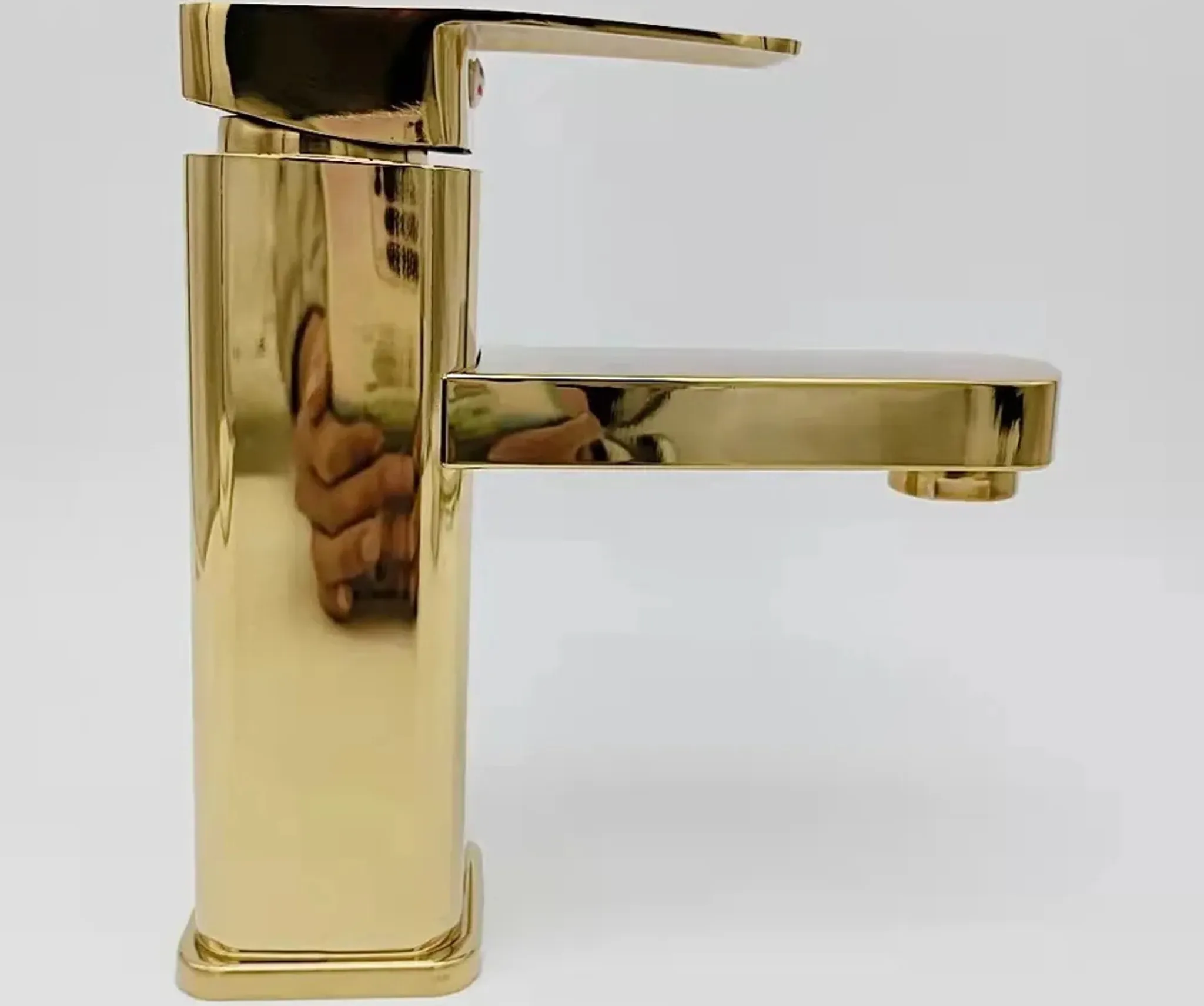 Ein glänzender goldener Wasserhahn mit rechteckiger Basis und Hebel.