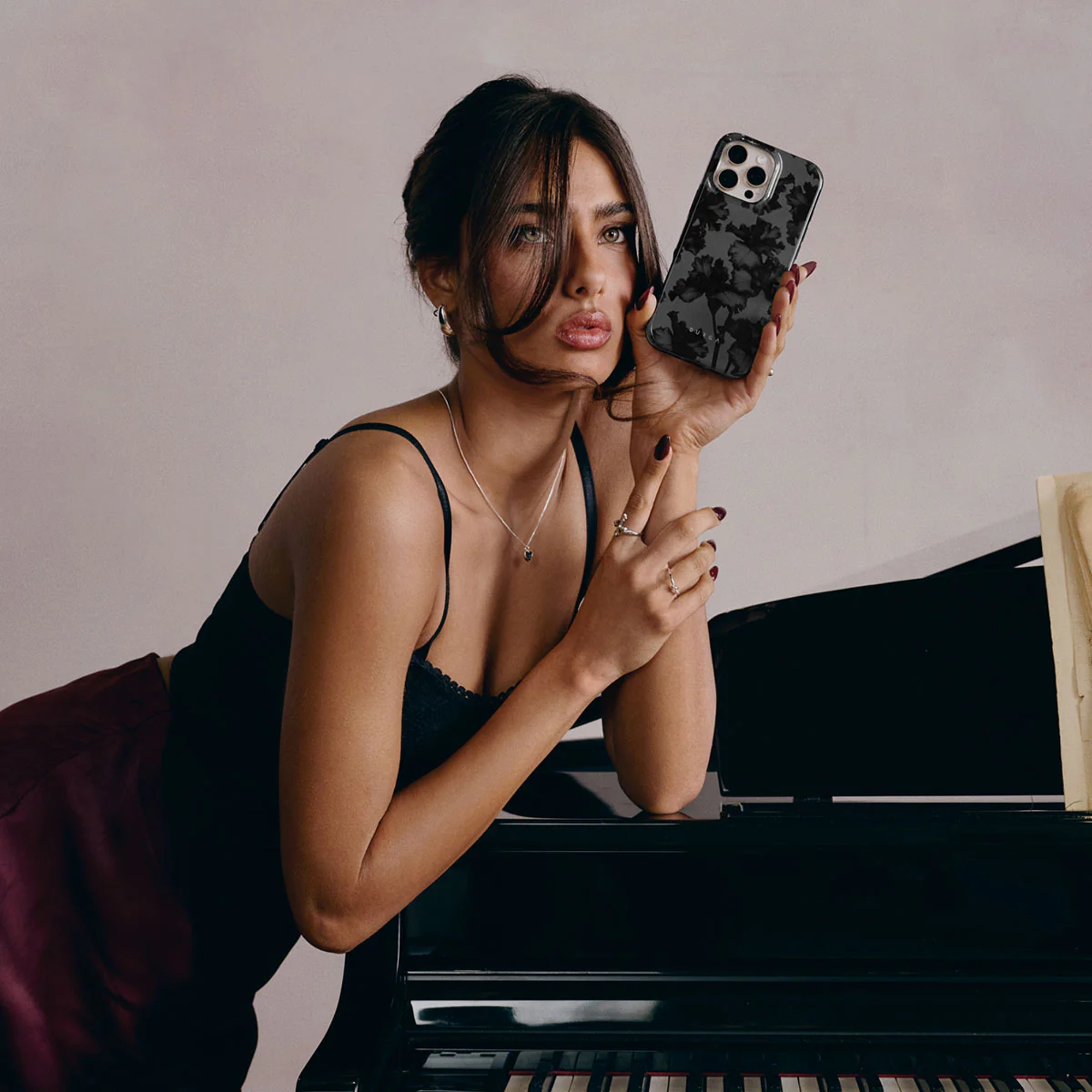 Een vrouw leunt op een piano en houdt een telefoon met bloemenpatroon vast.