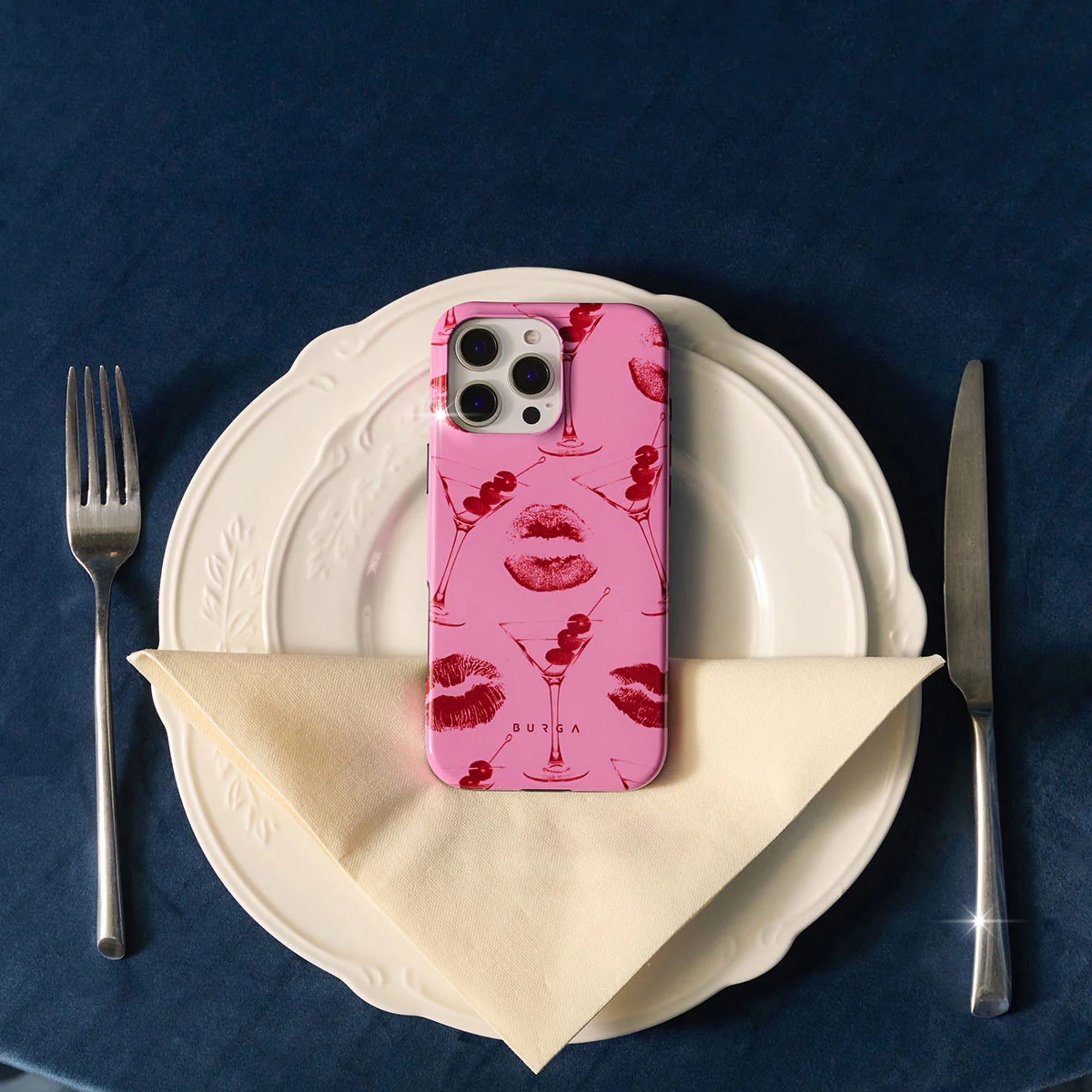 Een roze telefoonhoesje met lippen- en cocktailmotieven op een bord.