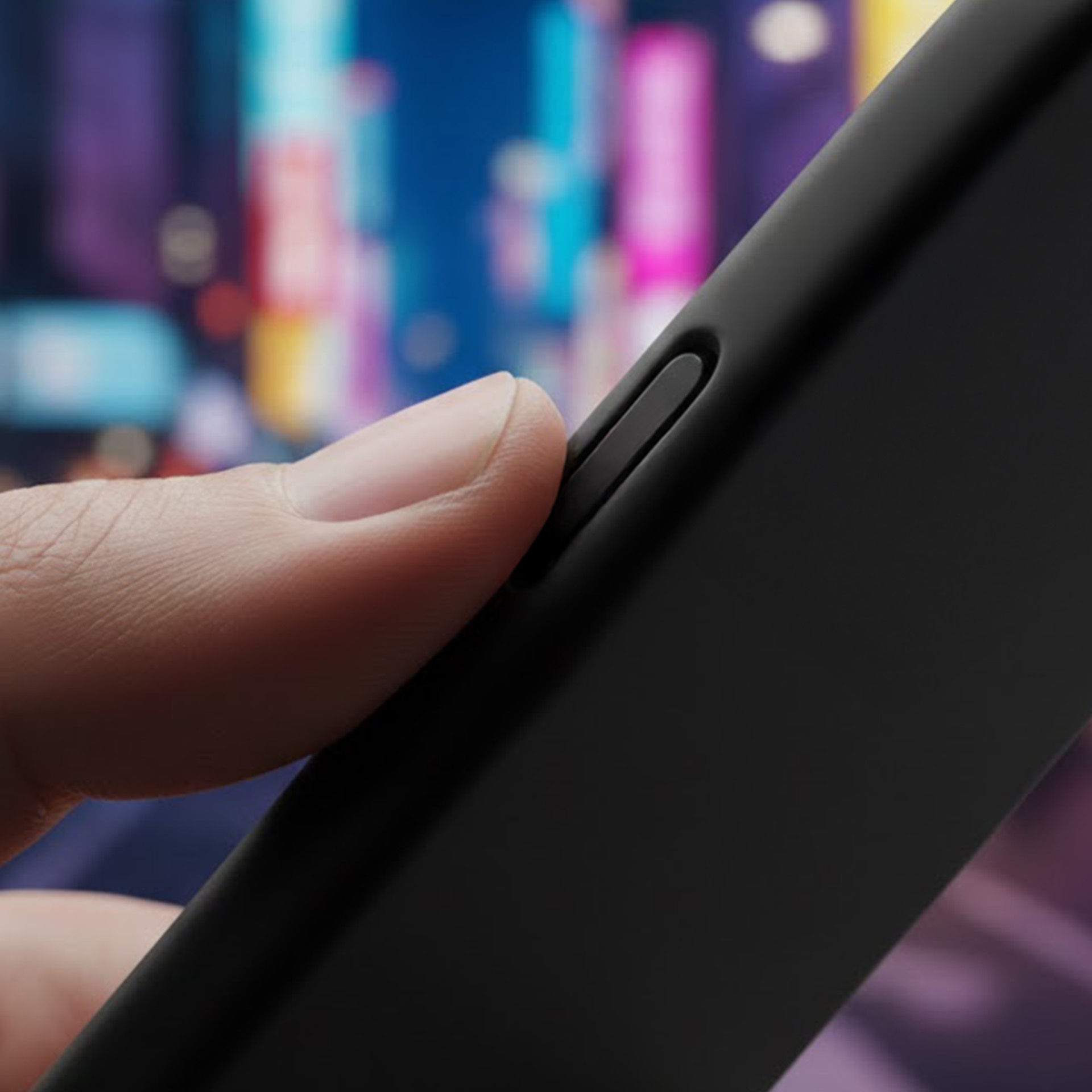 Palec naciska czarny przycisk na czarnym etui telefonu. Rozmazane światła.