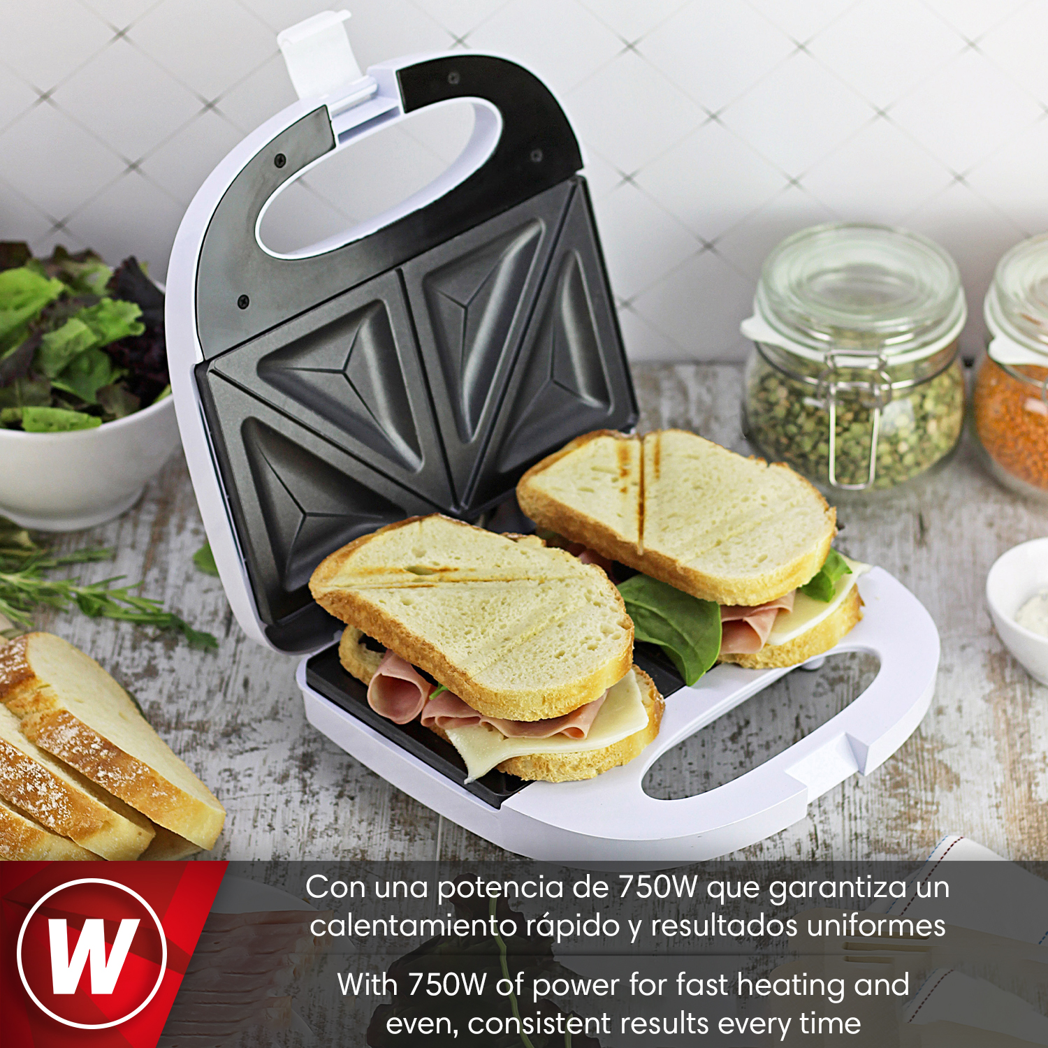 Sandwichera con dos sándwiches, pan y ensalada al fondo.