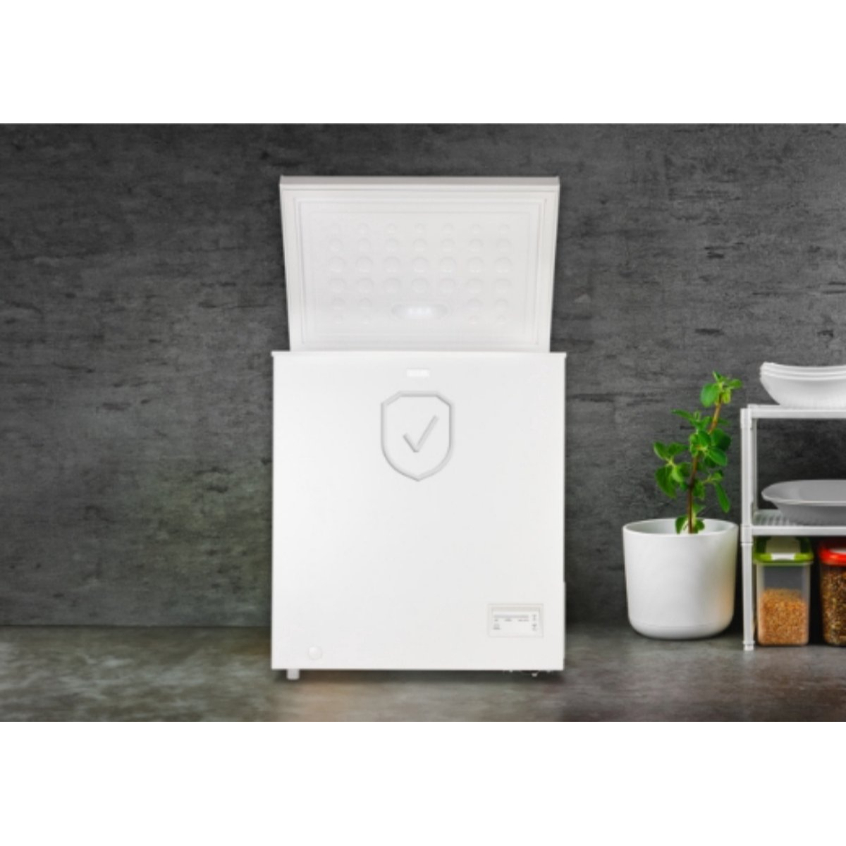 Biały zamrażarka skrzyniowa z otwartą pokrywą stoi przy betonowej ścianie.