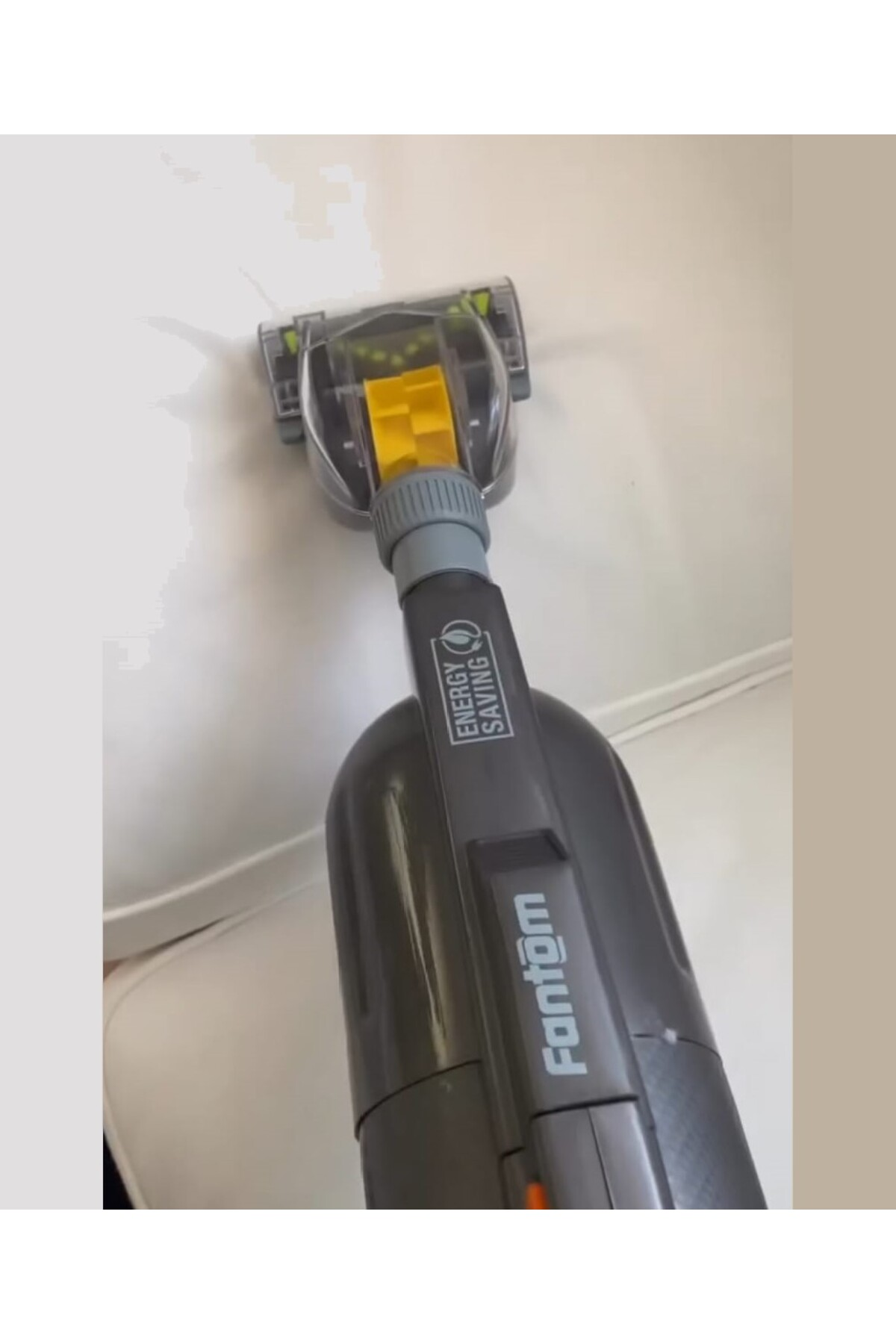 Sarı vurgulu gri bir Fantom elektrikli süpürge beyaz bir yüzeyi temizliyor.