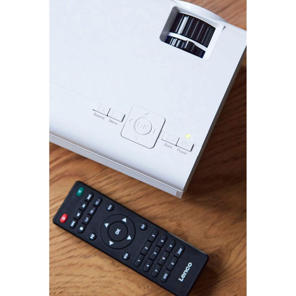 Biały projektor z pilotem na drewnianym stole.