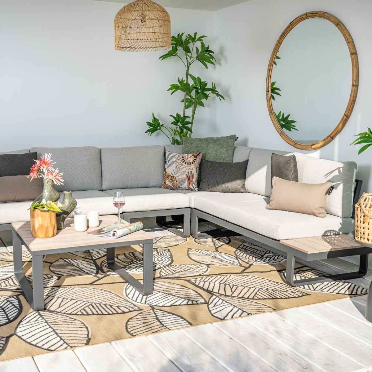 Un canapé sectionnel d'extérieur moderne avec coussins gris clair sur un tapis à motif de feuilles.