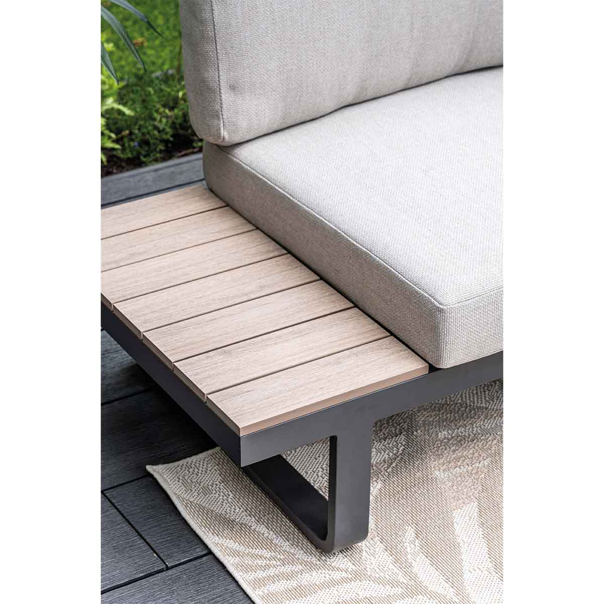 Canapé d'extérieur gris avec table d'appoint en bois et tapis.