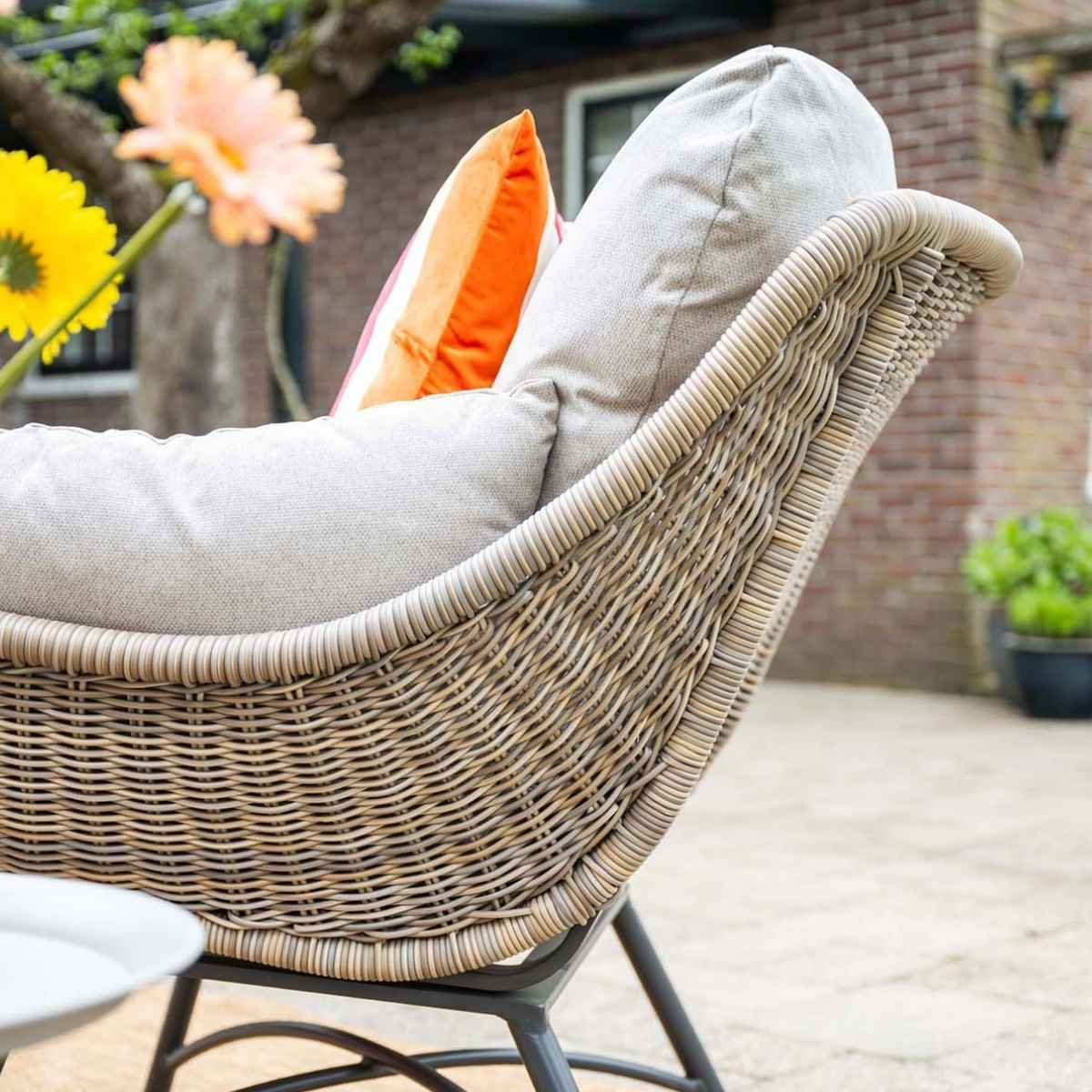 A rattan chair with cushions and flowers outdoors.