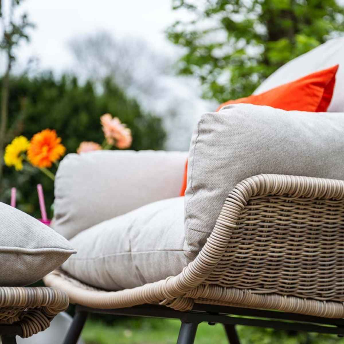 A beige cushion on a wicker chair with orange accents outdoors.
