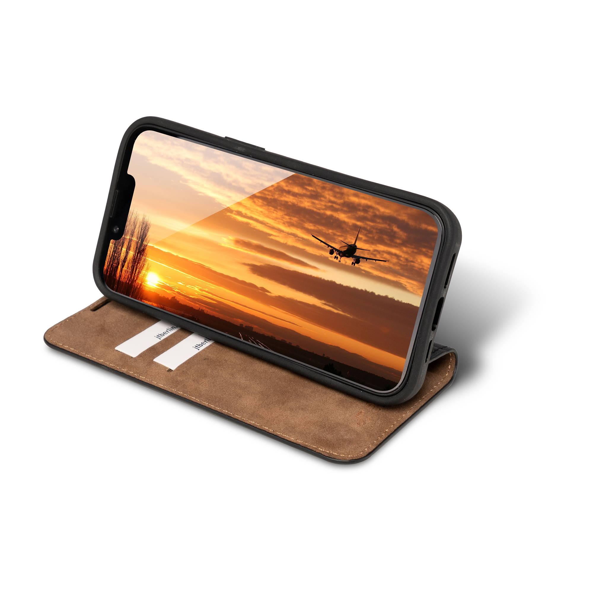 Ein Smartphone zeigt ein Flugzeug im Sonnenuntergang. Braune Hülle daneben.