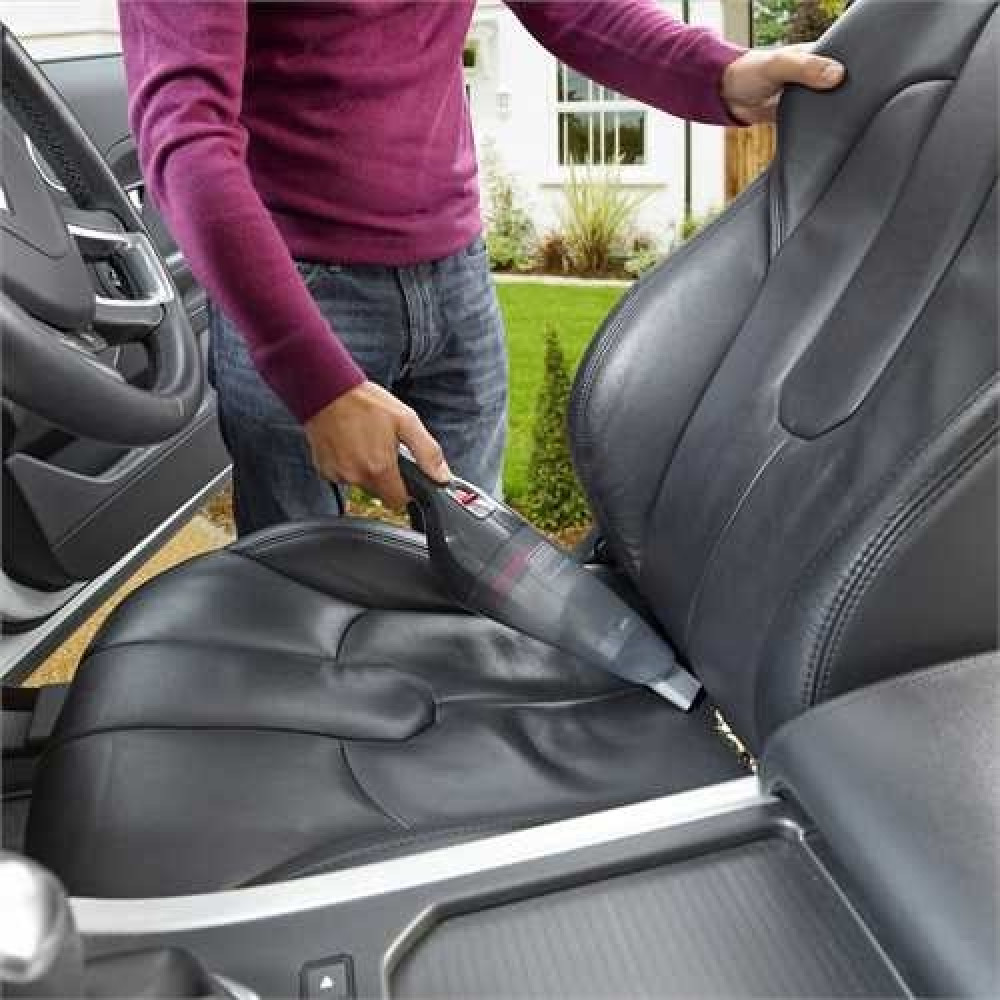 Osoba odkurza czarne siedzenie samochodu odkurzaczem ręcznym na zewnątrz.