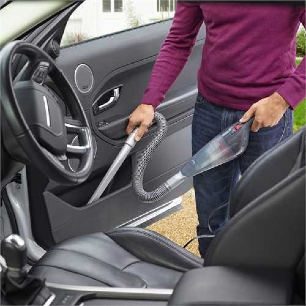 Osoba odkurza wnętrze samochodu odkurzaczem ręcznym.