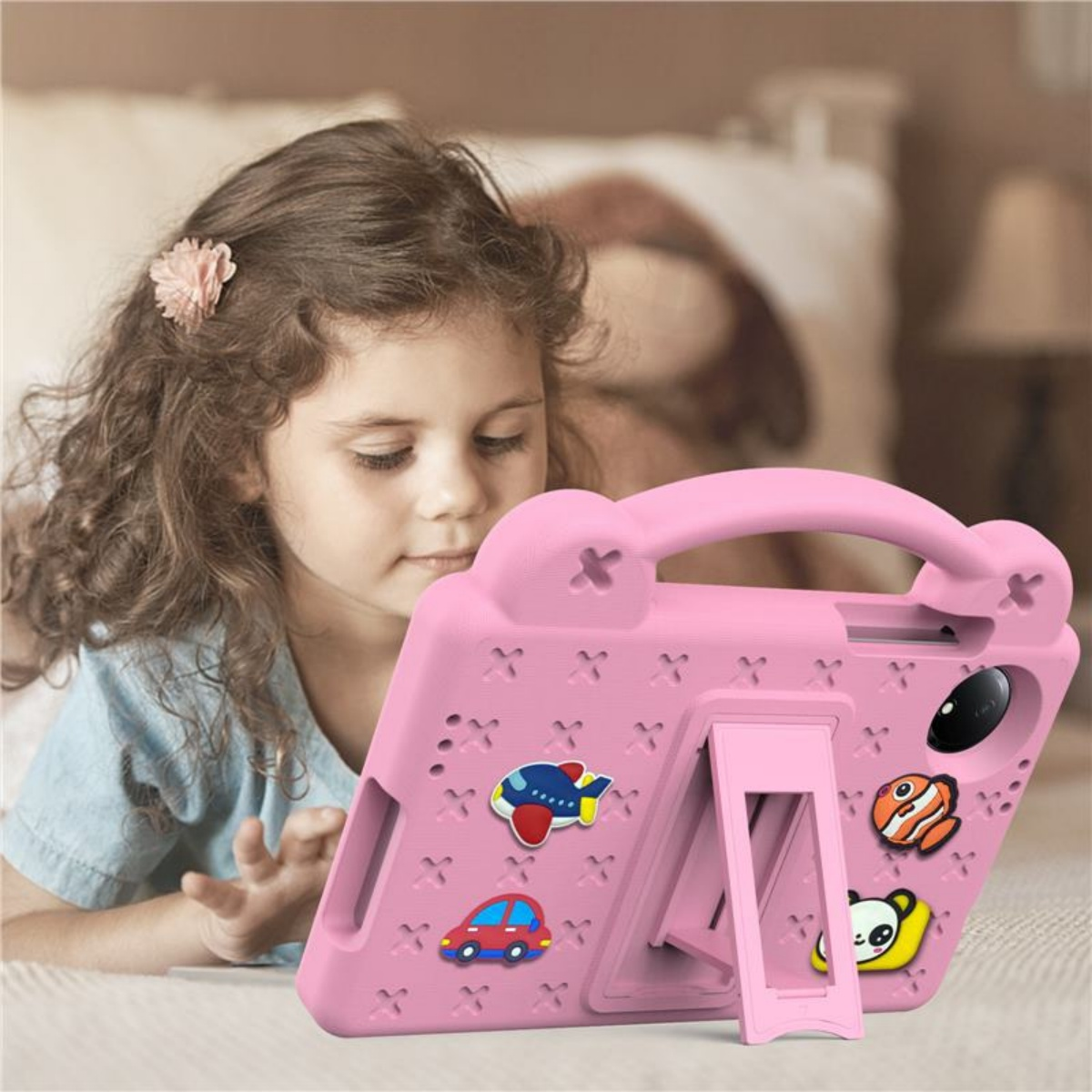 Ein rosa Tablet-Case mit niedlichen Aufklebern liegt auf einem Bett. Ein Mädchen schaut darauf.