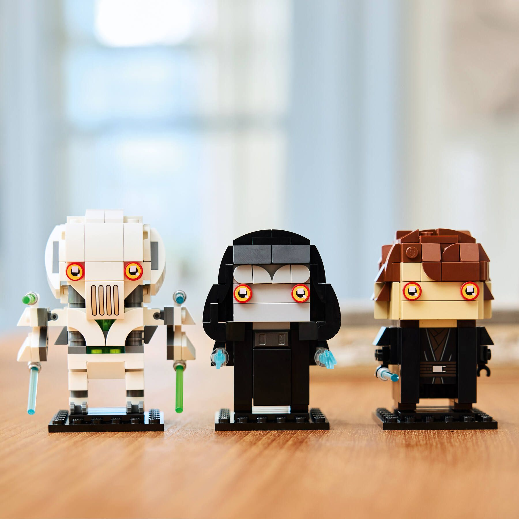 Üç Star Wars Lego figürü: Grevious, Palpatine ve Anakin ahşap masa üzerinde.