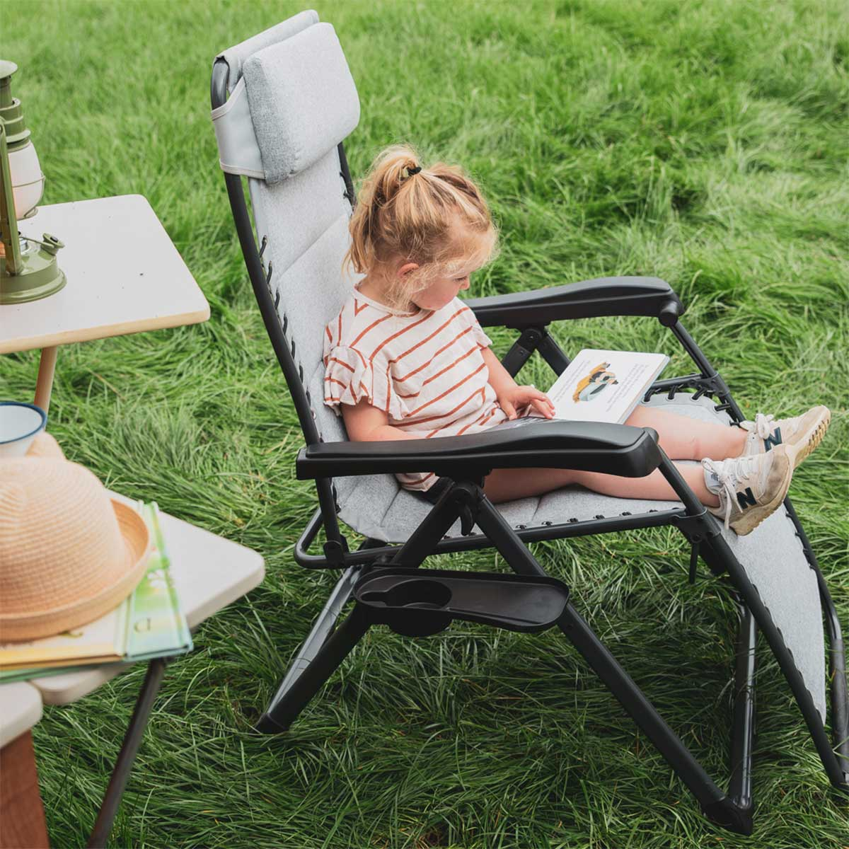 A young girl reads a book while sitting in an outdoor chair.