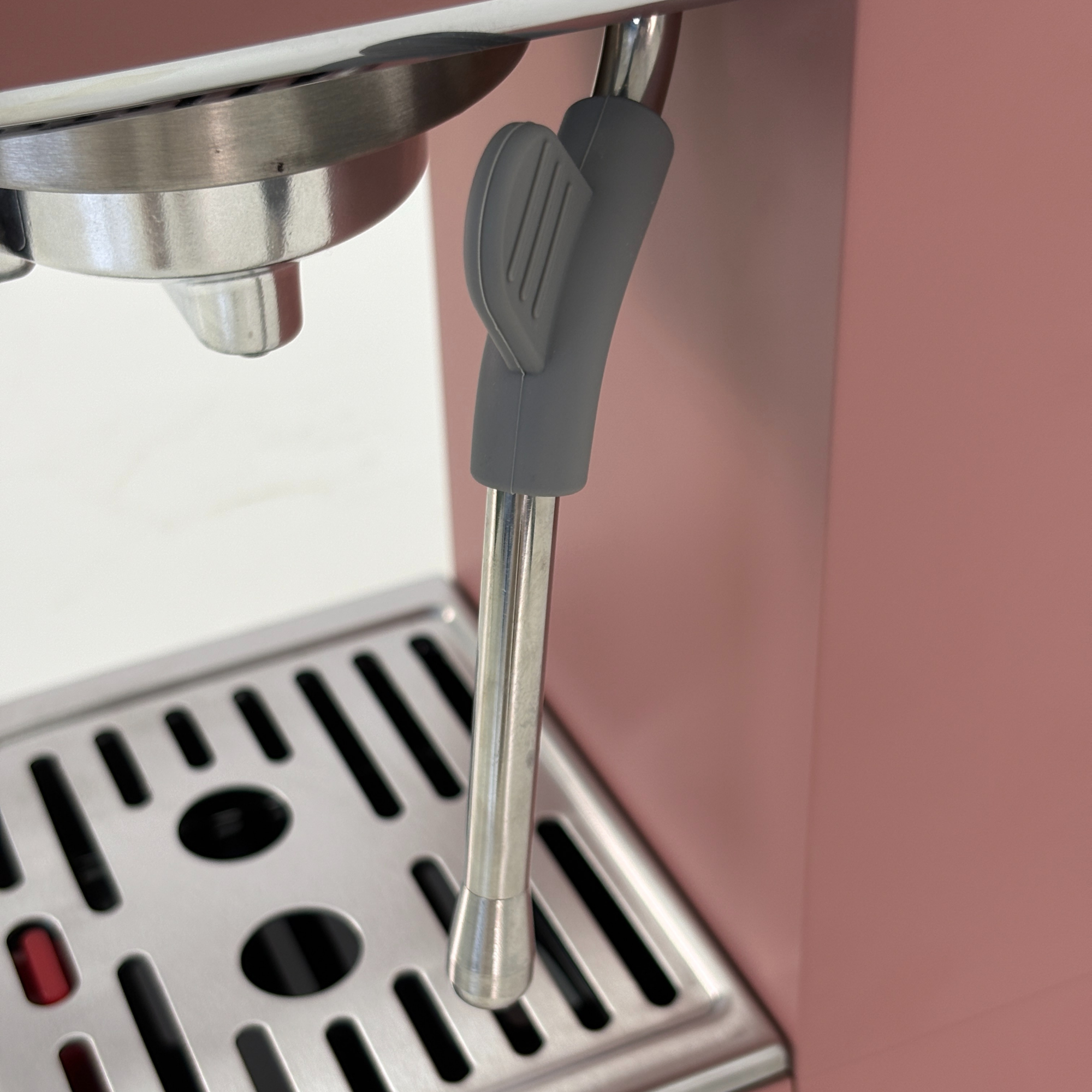 Primer plano de una cafetera rosa con varilla de vapor y bandeja de goteo.