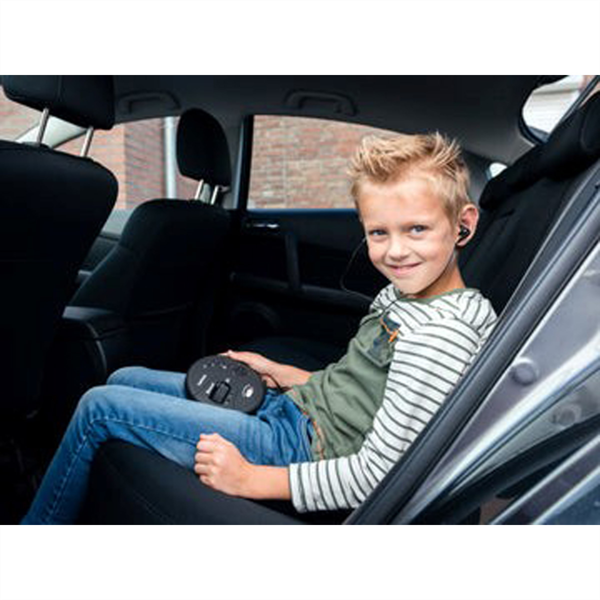 Chłopiec siedzi na tylnym siedzeniu samochodu, trzymając czarne urządzenie.