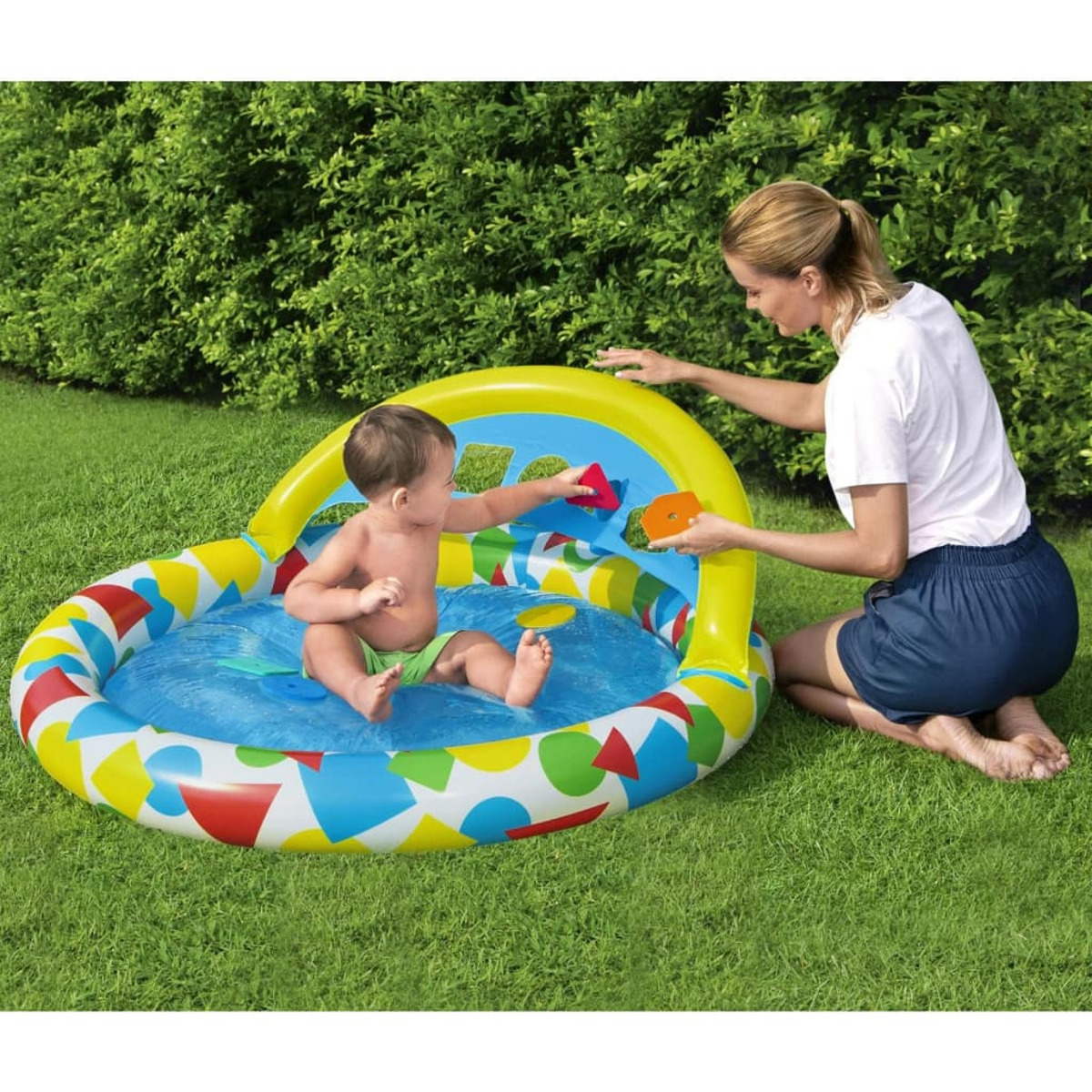 Baby in buntem aufblasbarem Pool mit Mama spielt draußen im Gras.