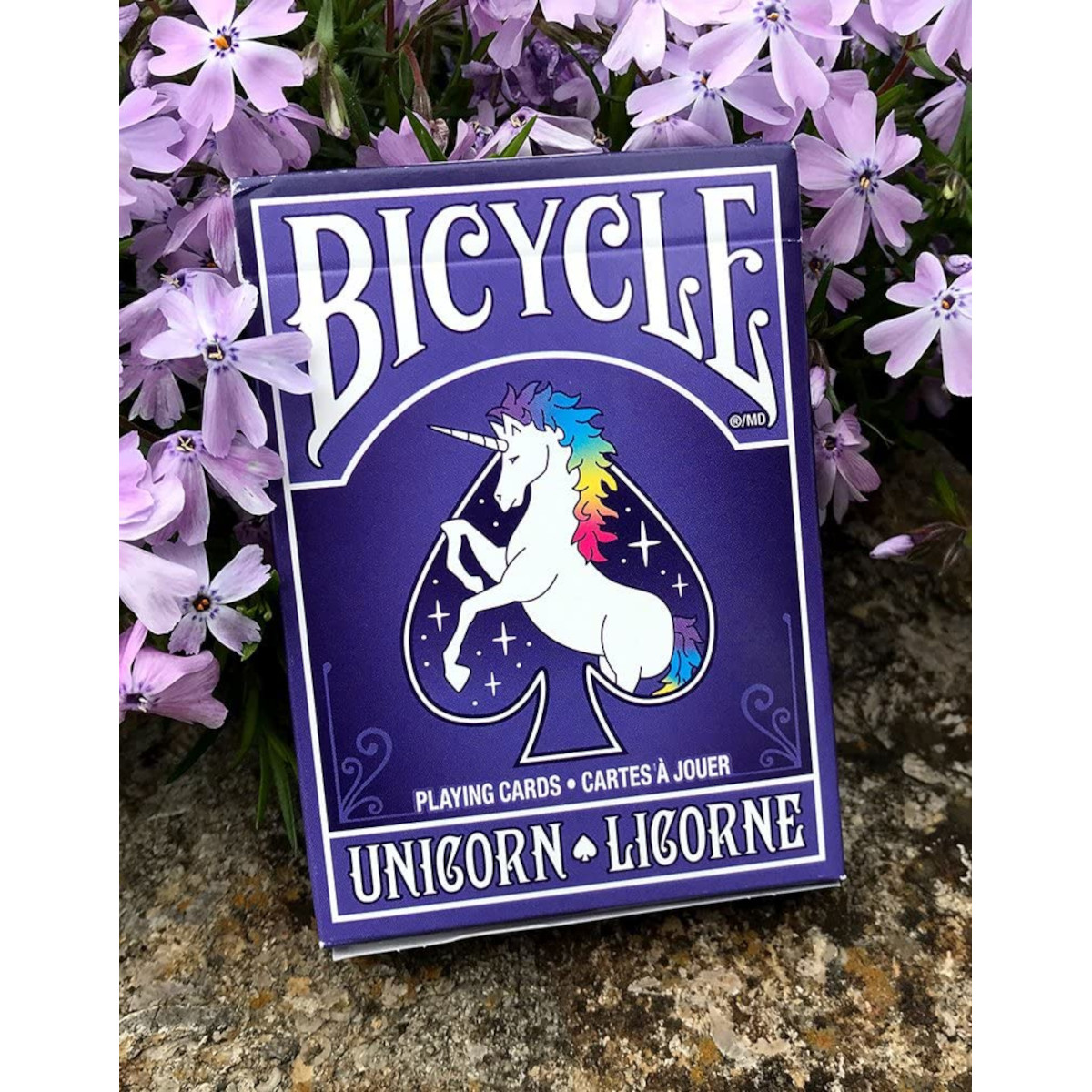 Ein violettes Bicycle-Kartenspiel mit einem Einhorn und Regenbogenmähne vor lila Blüten.