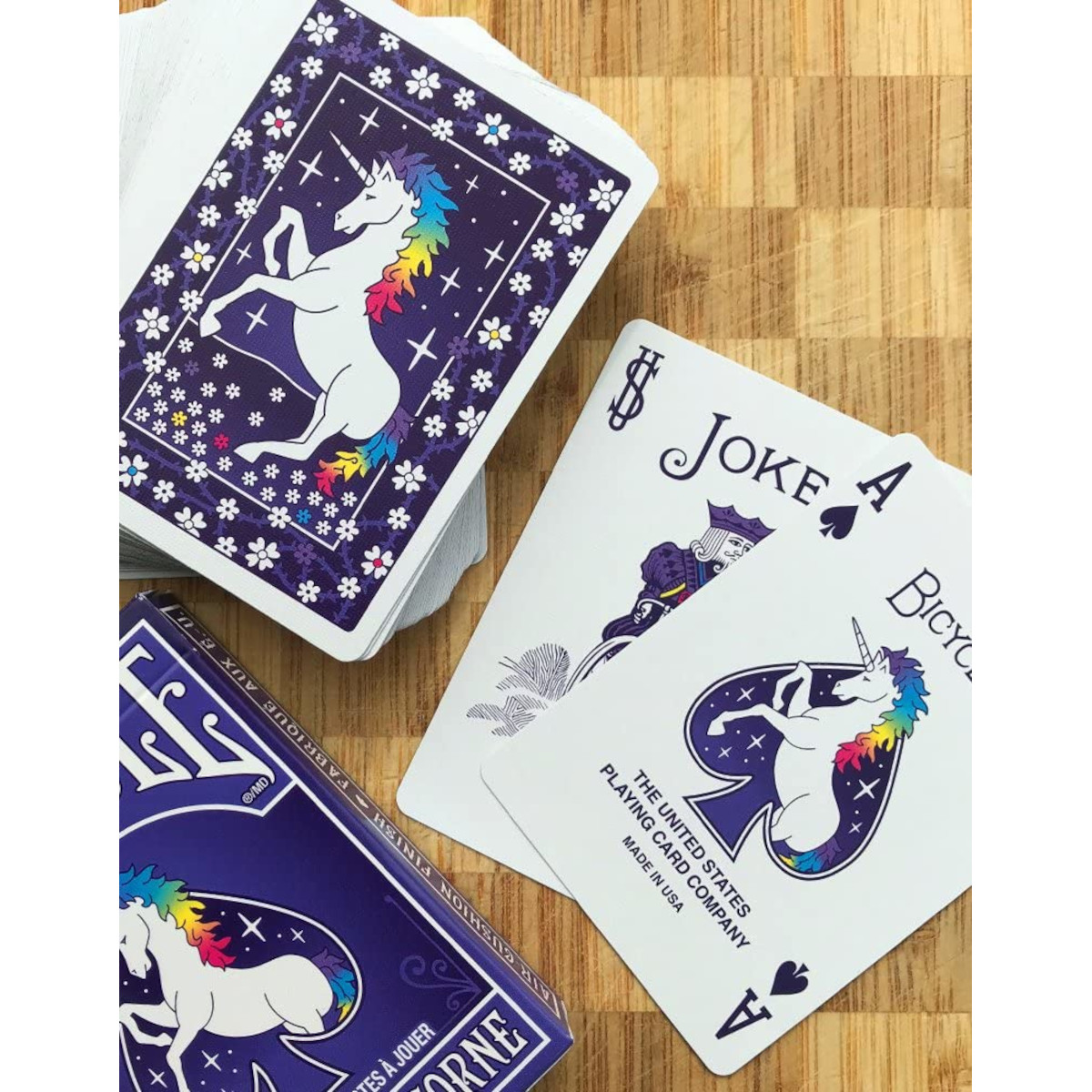 Ein Kartenstapel mit Einhorn-Motiv, zwei Joker und eine Spielkarte liegen auf Holz.