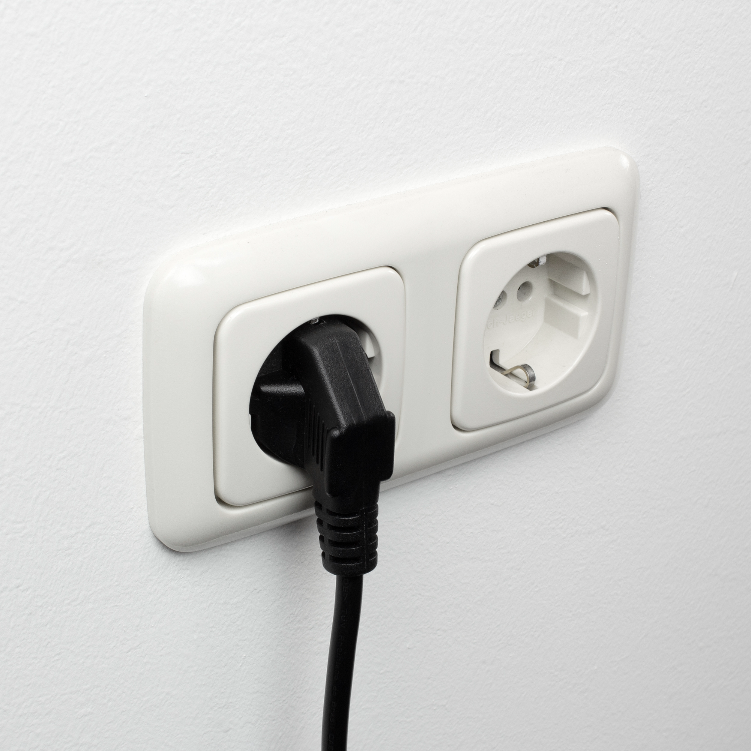 Ein schwarzer Stecker steckt in einer weißen Steckdose an einer weißen Wand.