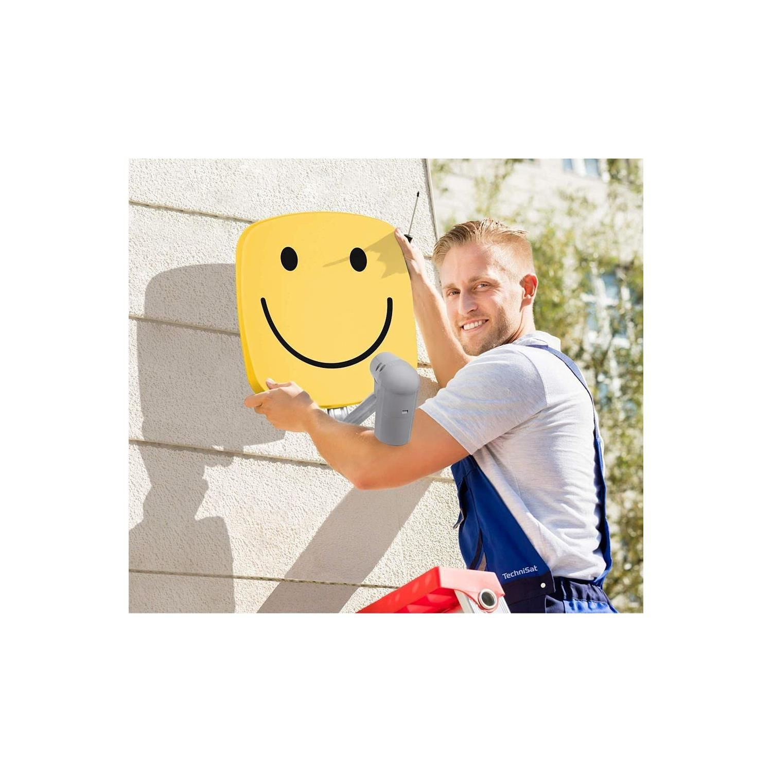 Mann montiert gelbes Smiley-Schild mit Schraubenzieher an Hauswand. Leiter steht daneben.