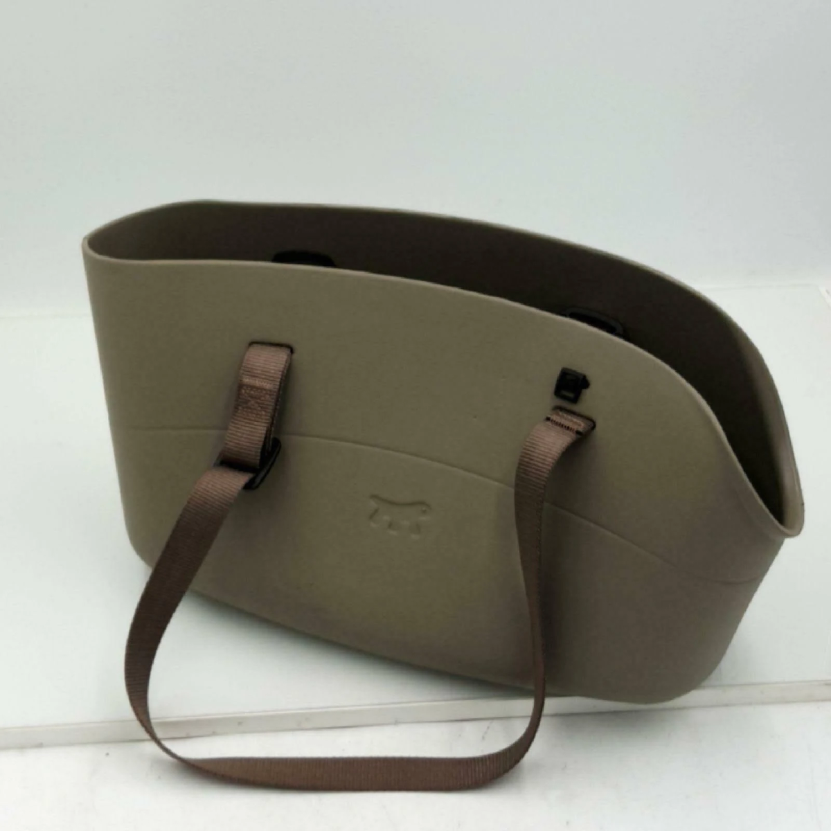 Eine taupefarbene Tasche mit braunen Trägern und einem Prägelogo.