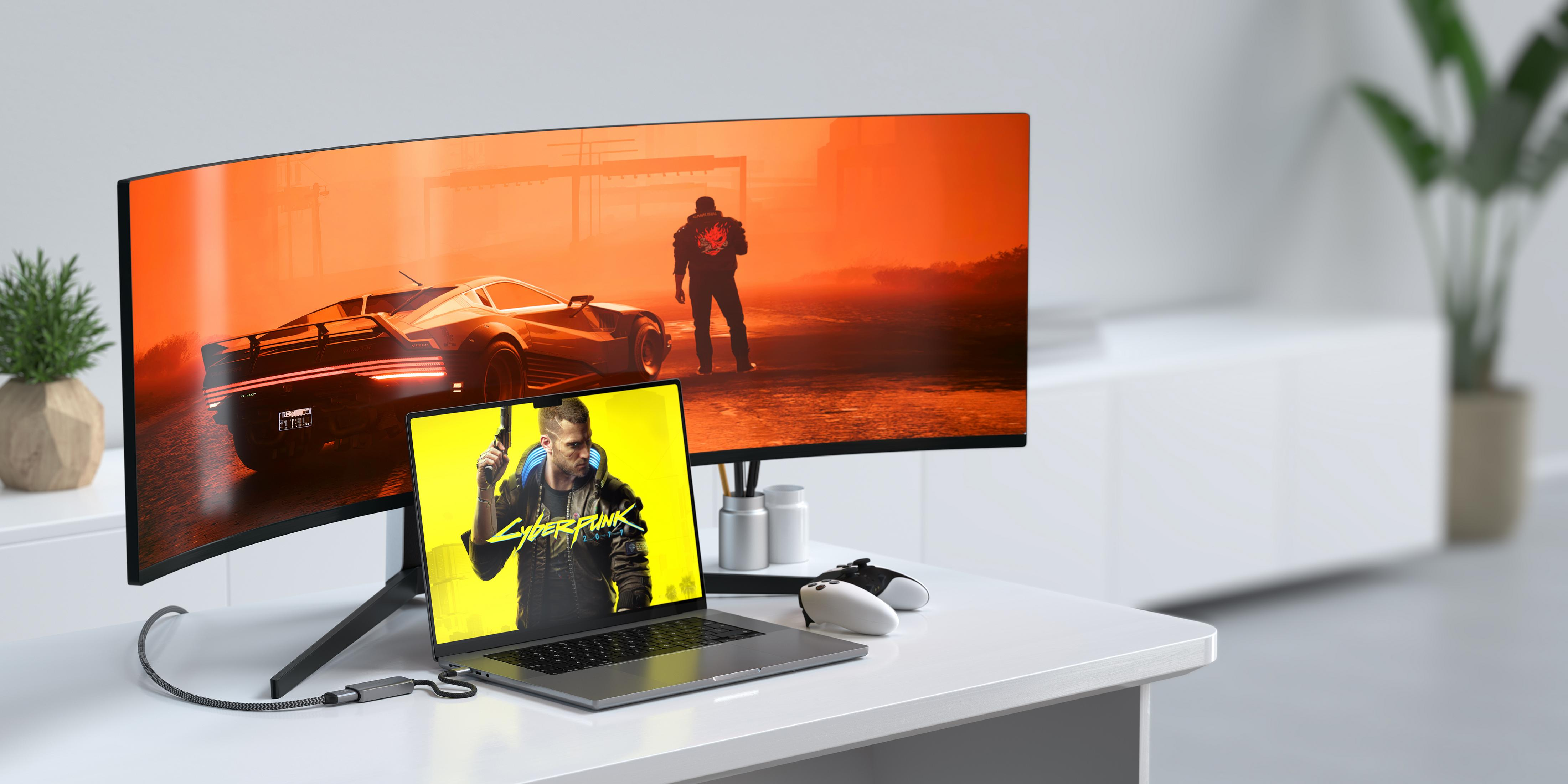 Un laptop mostra Cyberpunk 2077, collegato a un grande monitor curvo.
