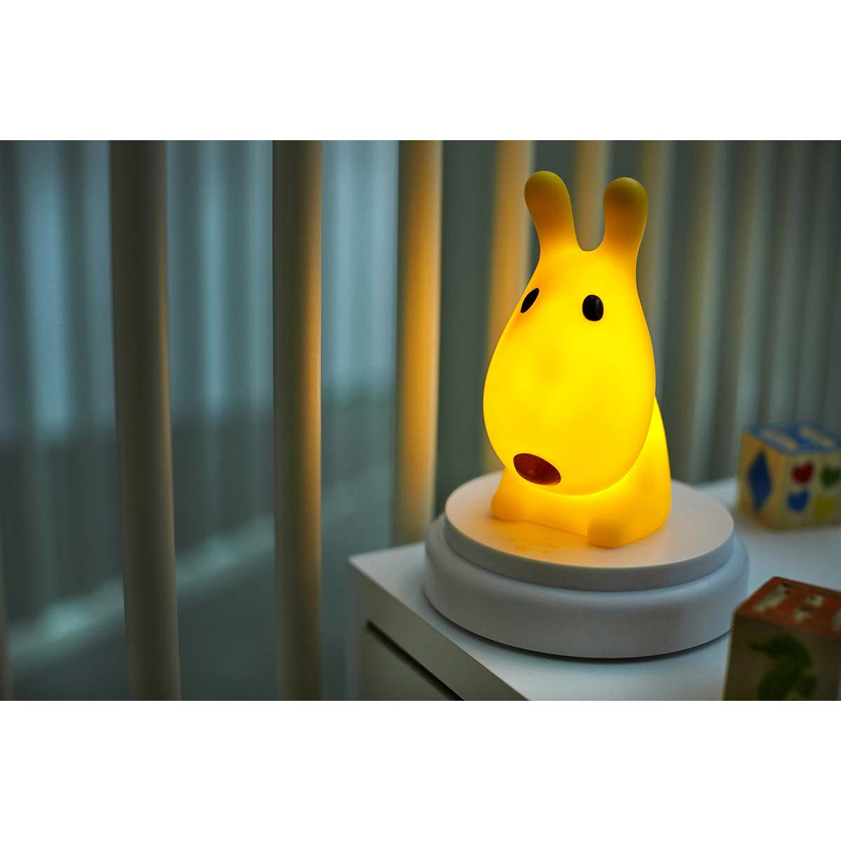 Una luz de conejo amarilla brilla en una mesita de noche junto a bloques de juguete.