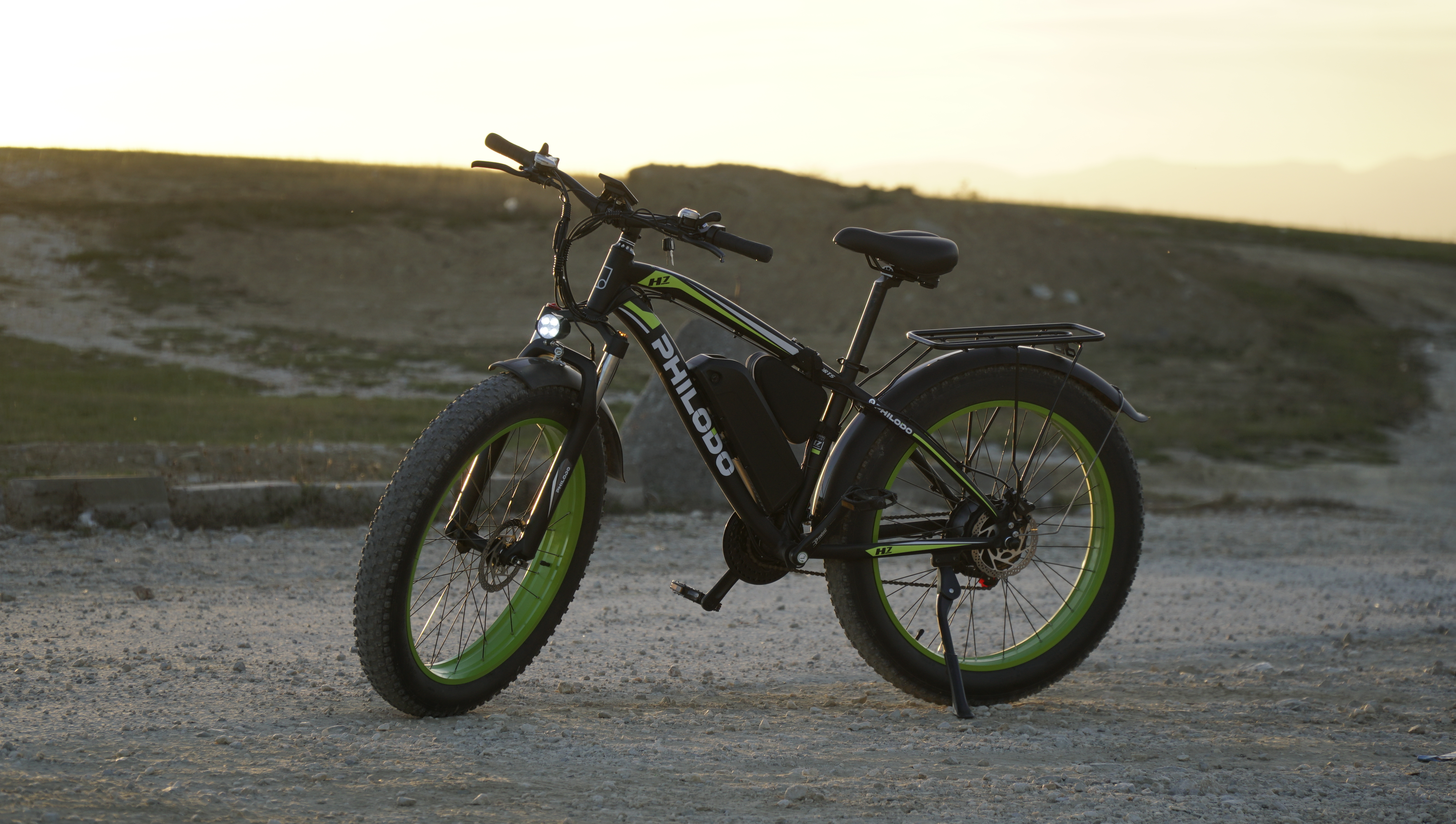 Bici elettrica nera con cerchi verdi parcheggiata sulla ghiaia. Luce del tramonto.