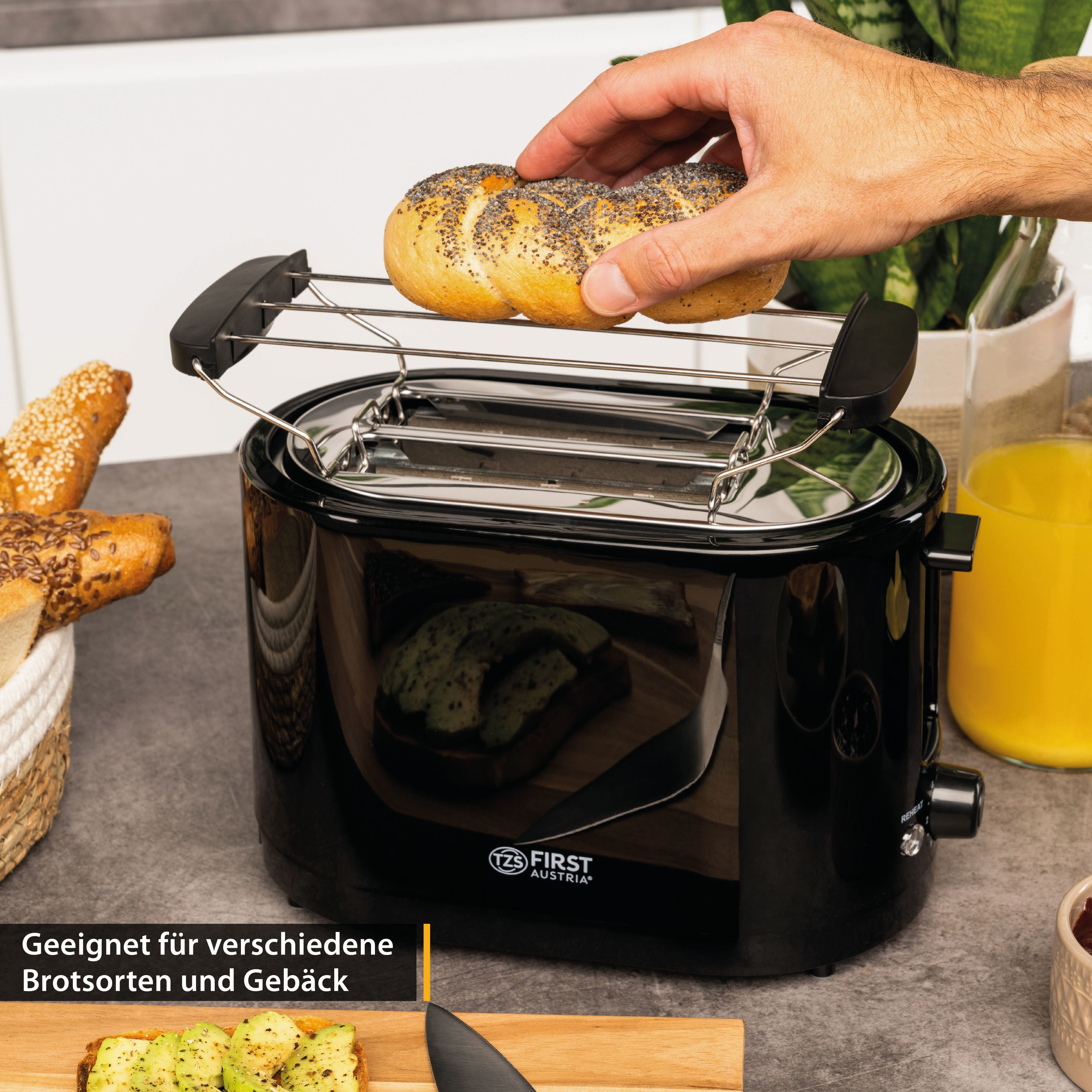 Eine Hand legt ein Brötchen mit Mohn auf einen Toaster. Daneben liegen Brote und Saft.