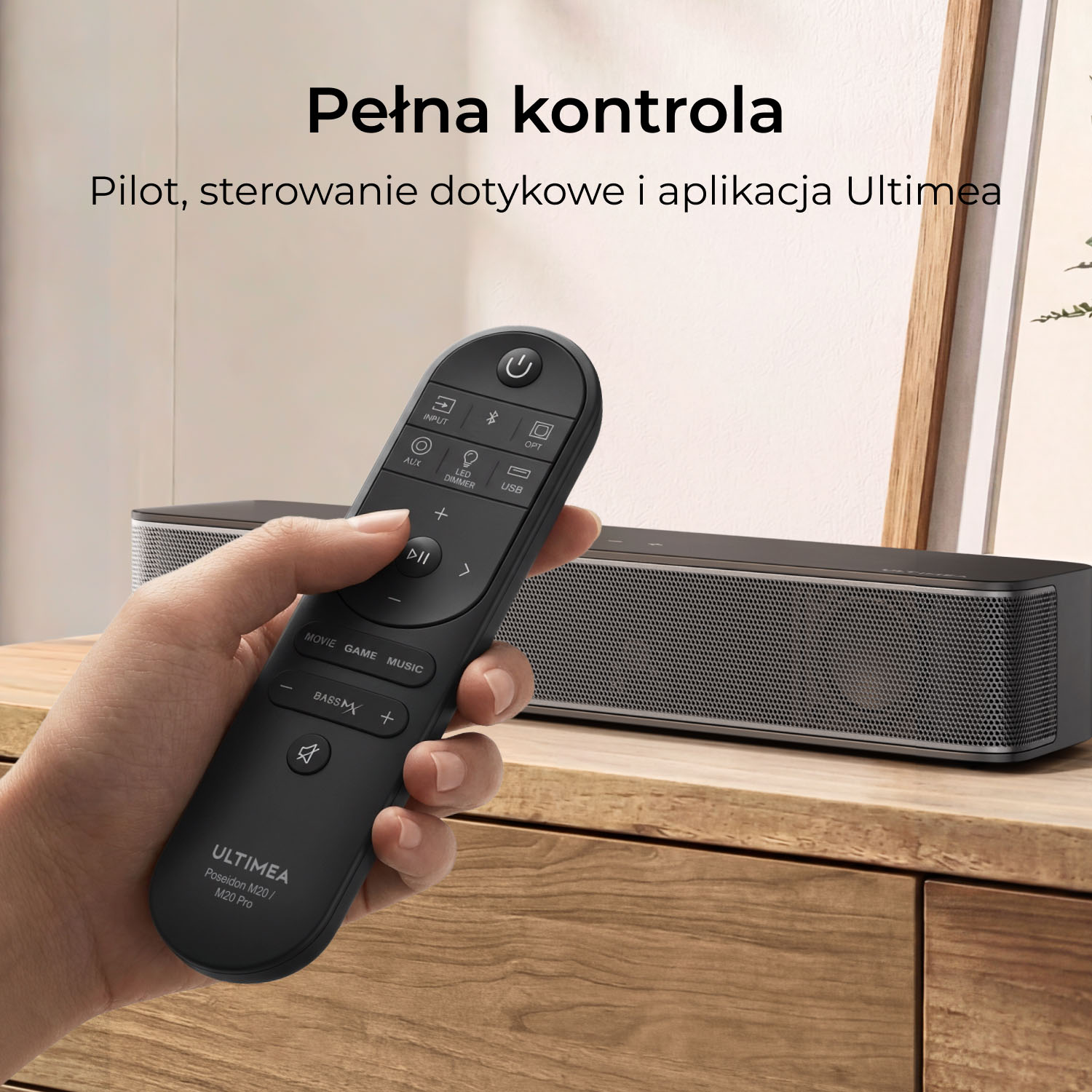 Dłoń trzyma czarny pilot przed soundbarem na drewnianej powierzchni.
