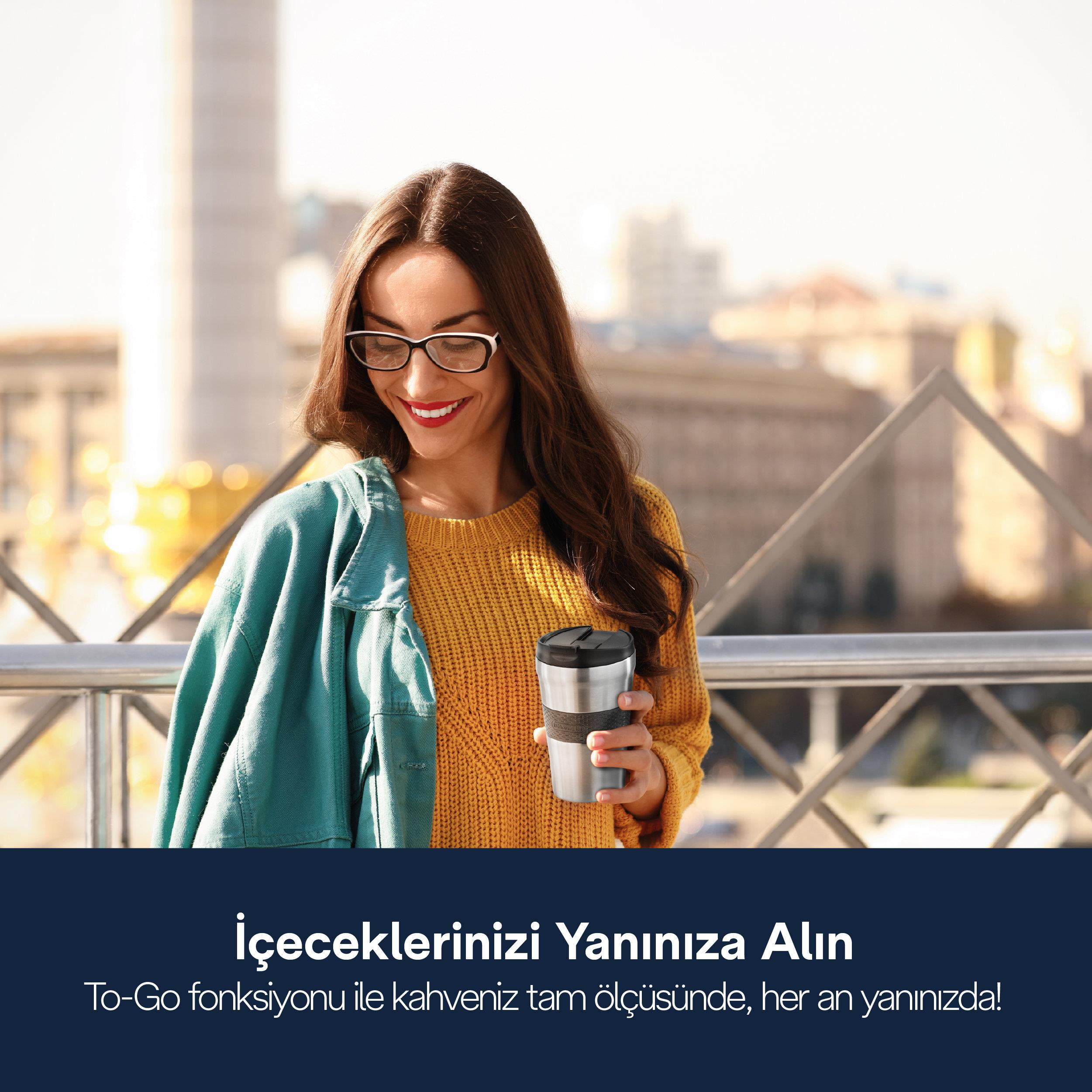 Gözlüklü kadın, sarı kazak giymiş, gümüş rengi kupa tutuyor.