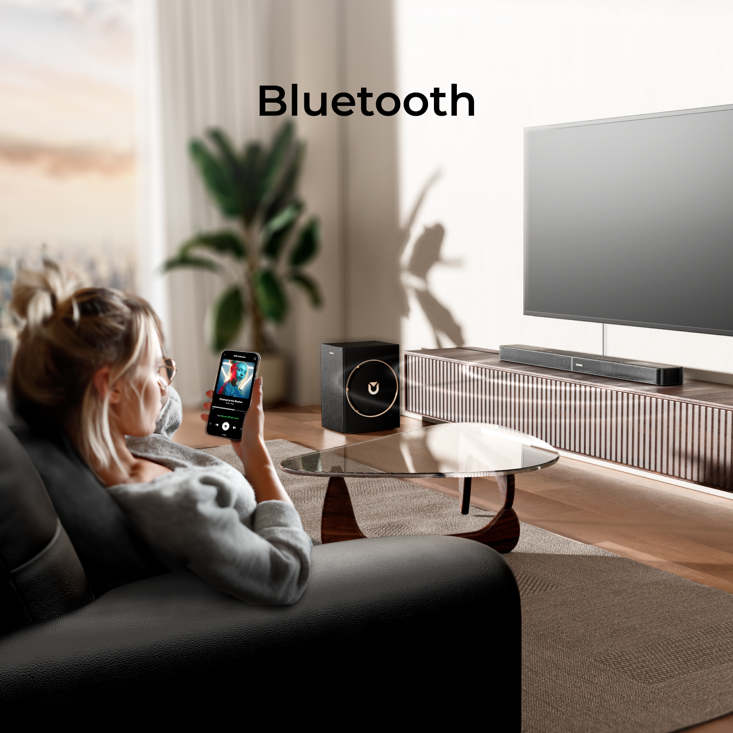 Kobieta na kanapie z telefonem, TV, soundbar, subwoofer, stolik kawowy, roślina.