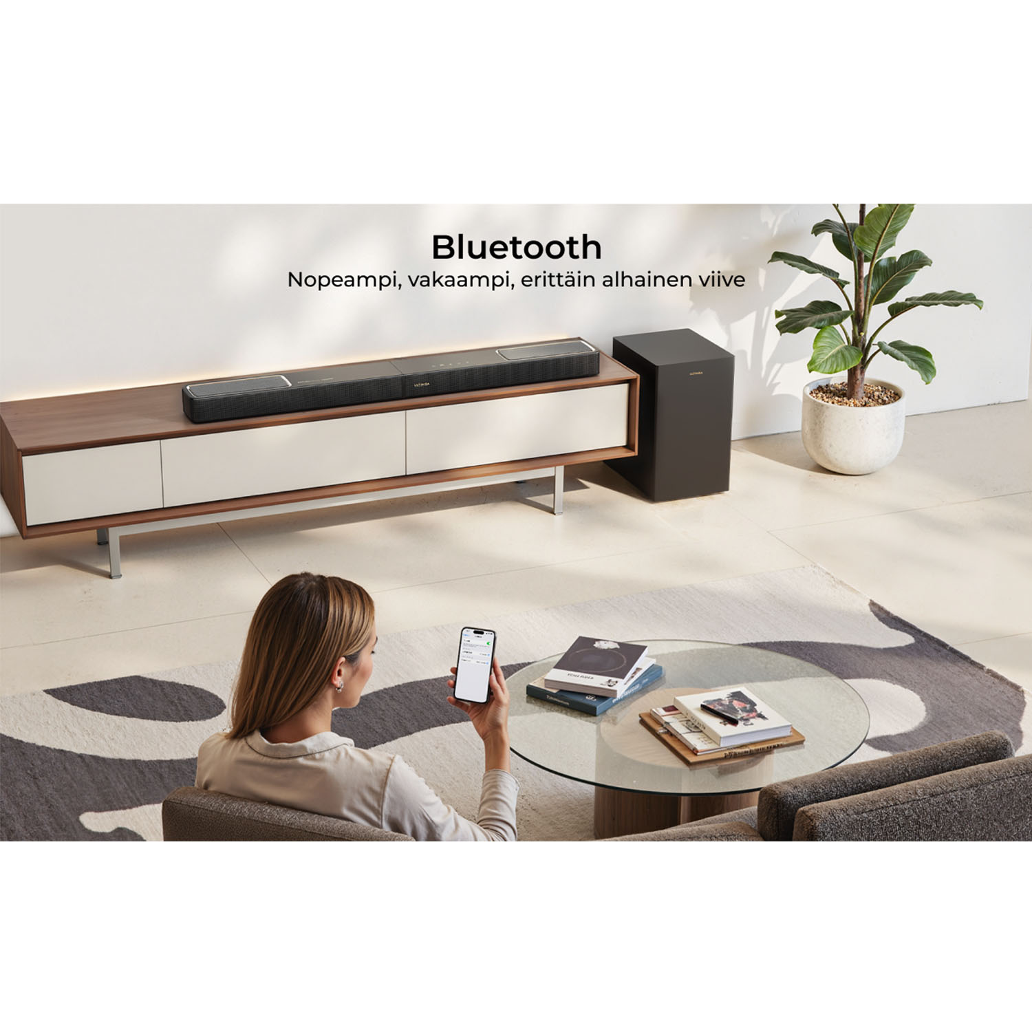 Een vrouw houdt een smartphone vast en kijkt naar een geluidssysteem, subwoofer en tv-meubel.
