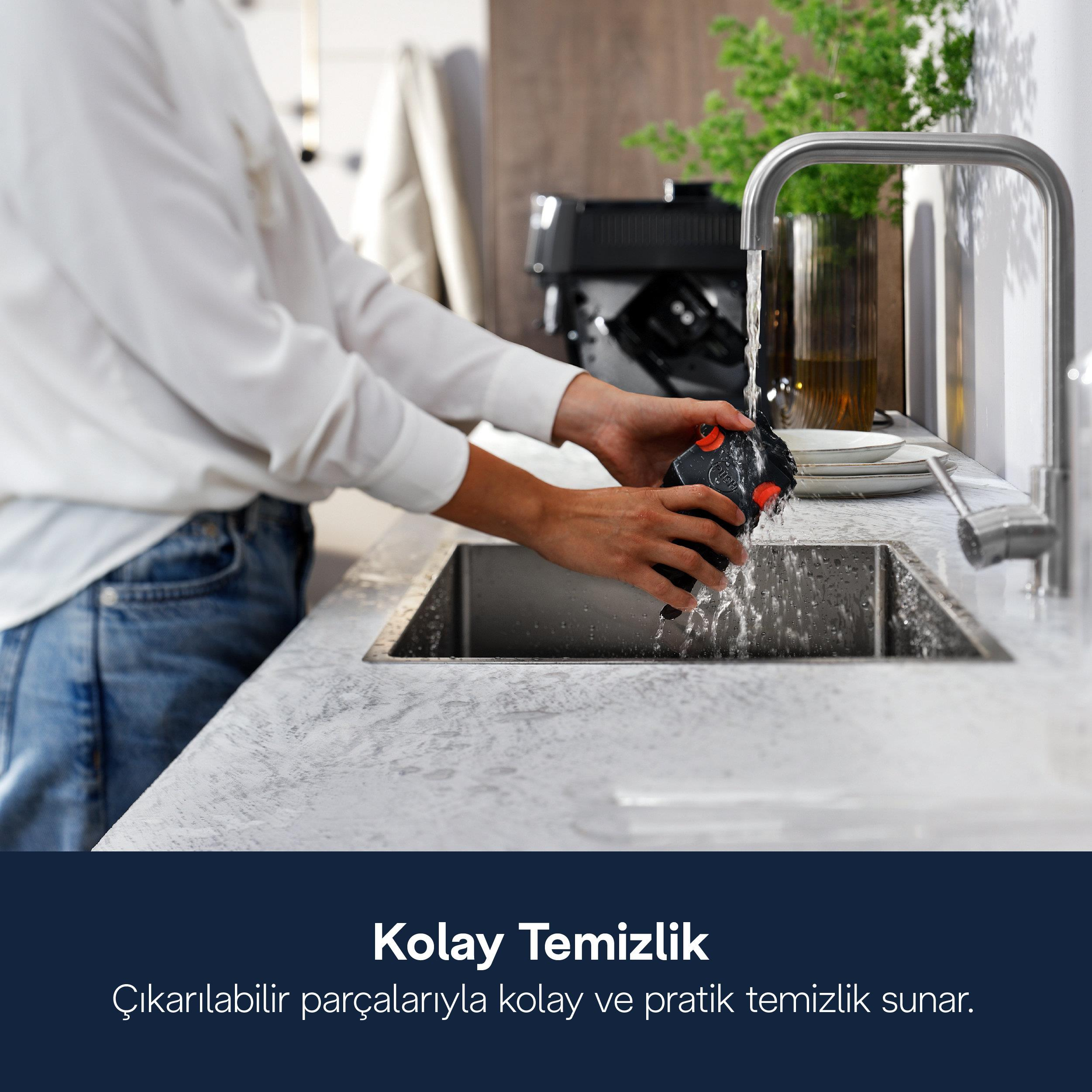 Osoba myje czarną część z czerwonym przyciskiem pod bieżącą wodą w zlewie.