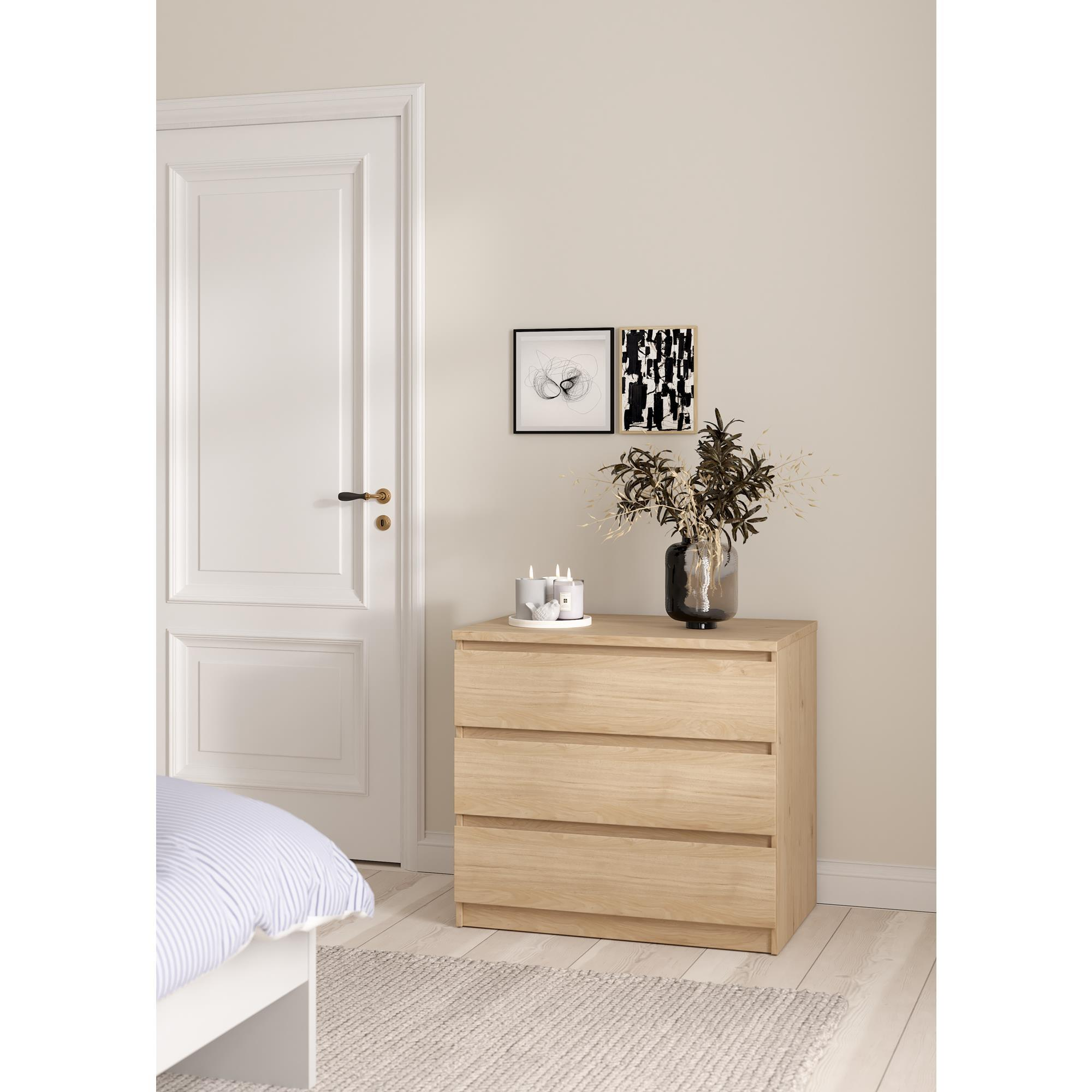 Un dormitorio luminoso con cómoda de madera, ropa de cama a rayas y puerta blanca.
