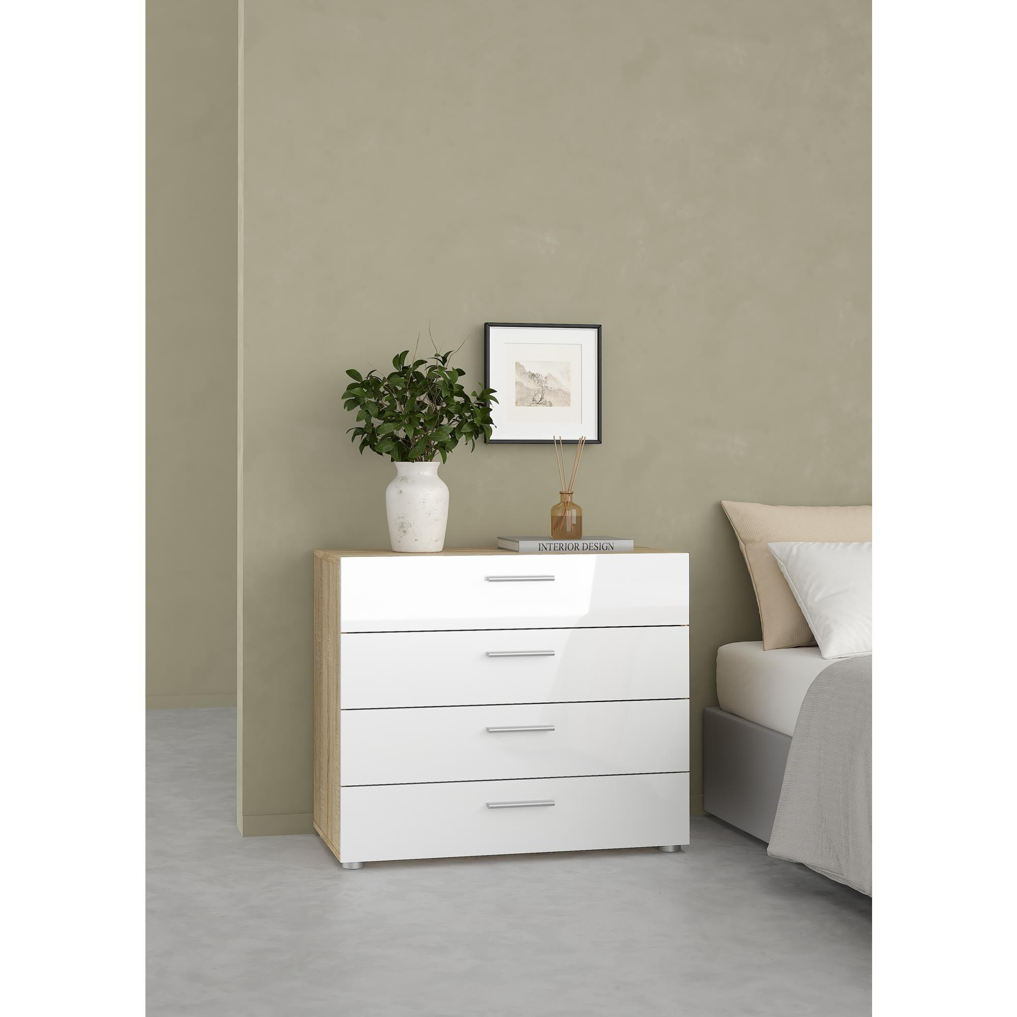 Una cómoda blanca con tapa de madera junto a una cama. Decorada con un jarrón y un libro.